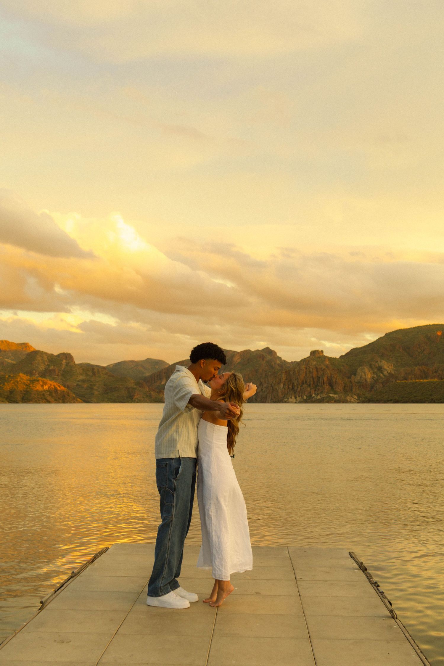 A romantic sunset moment on a wooden pier overlooking mountains and water.