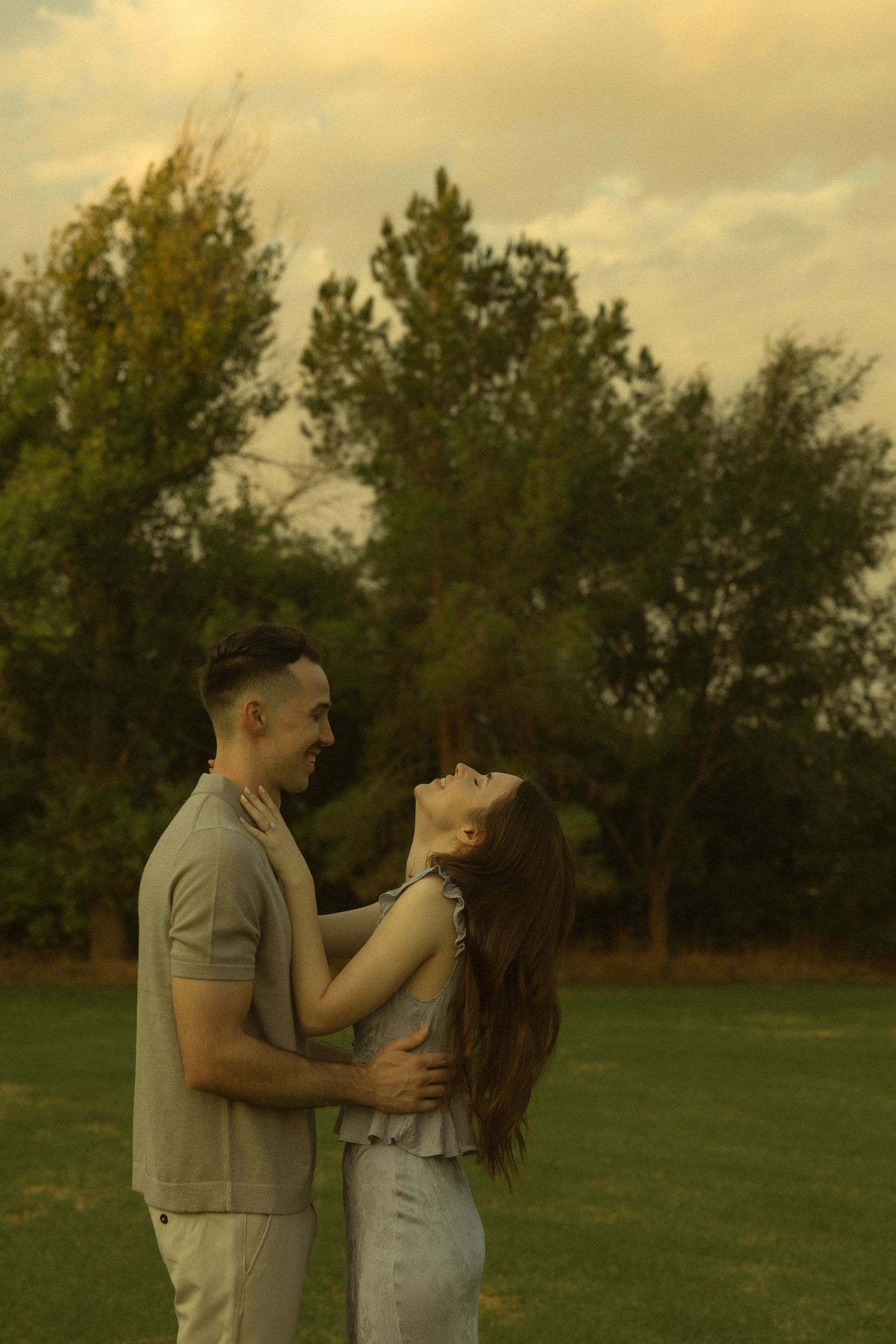 A romantic couple embracing and laughing together in a park during a golden sunset.