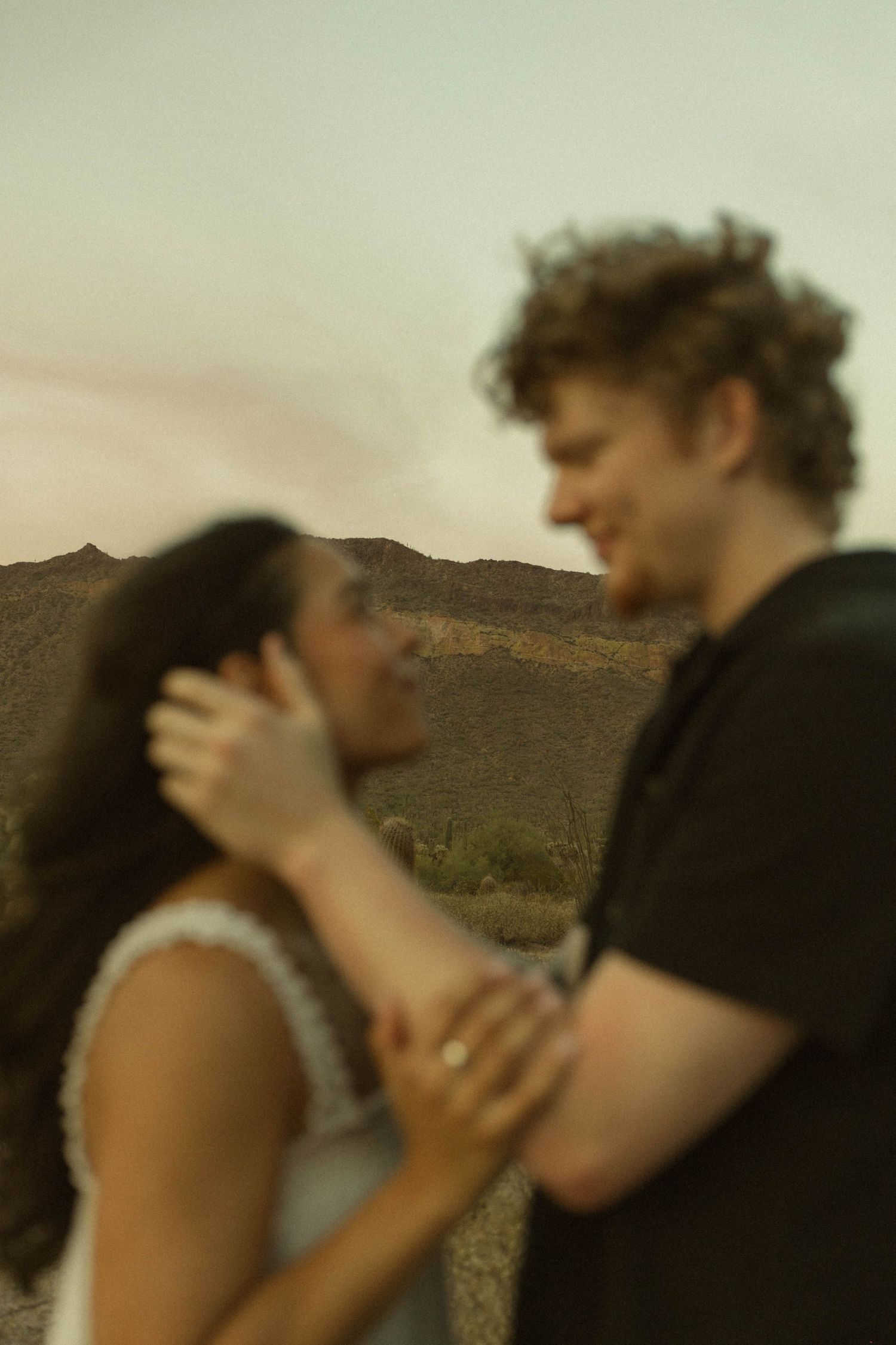Blurred couple sharing a romantic moment in a desert landscape with mountains at sunset.