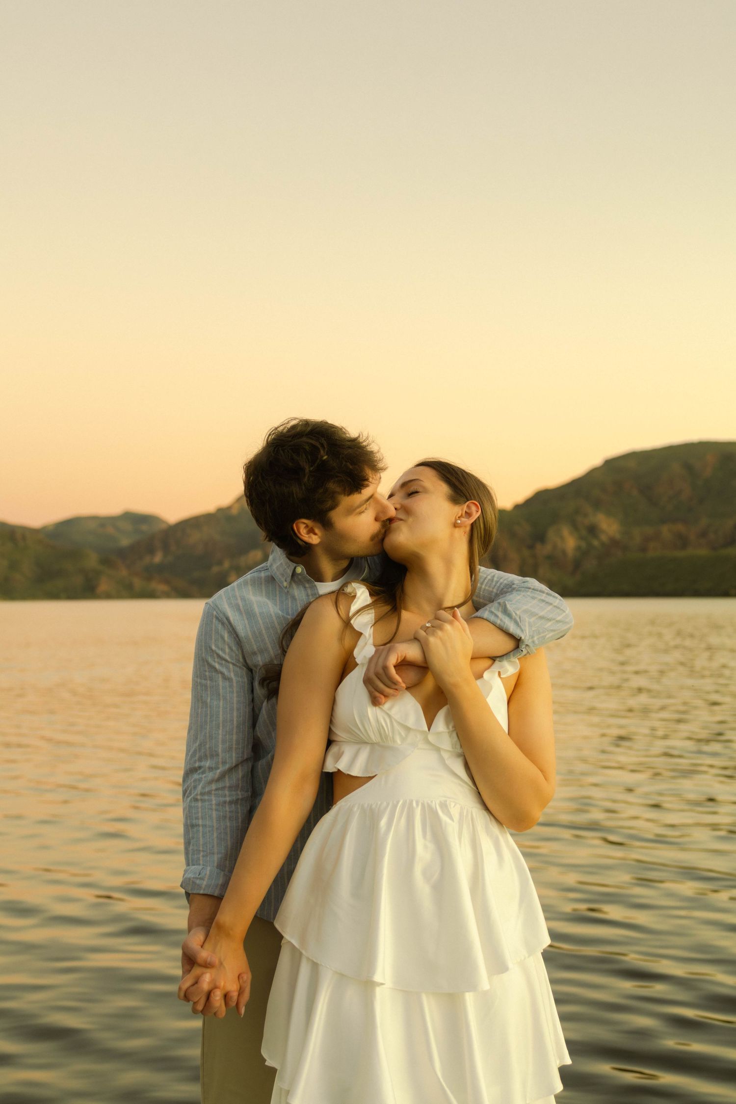 An intimate couple's portrait by the water during sunset with mountains on the horizon.