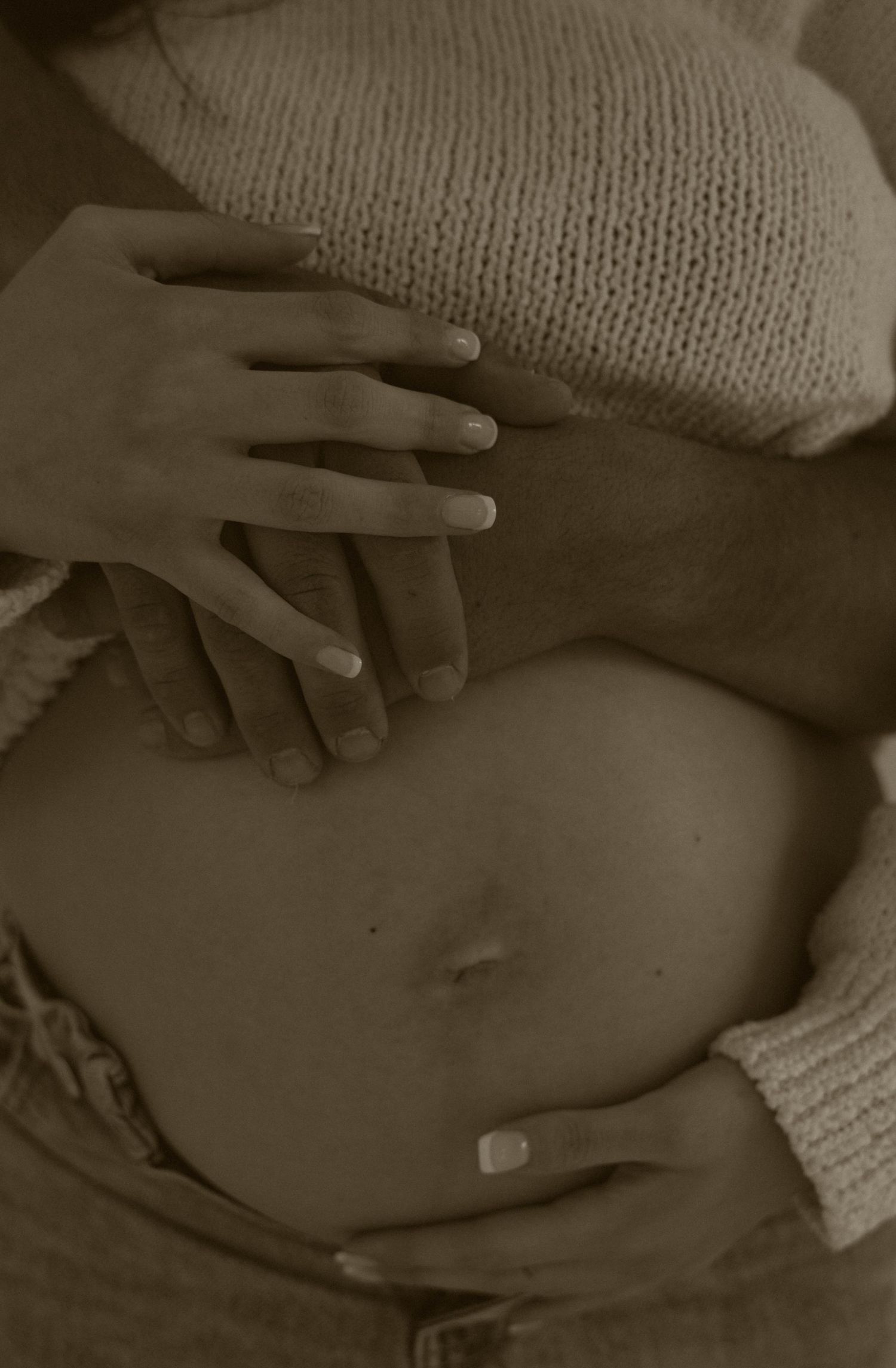 A series of black and white images showing hands gently resting on a pregnant belly in a sweater.
