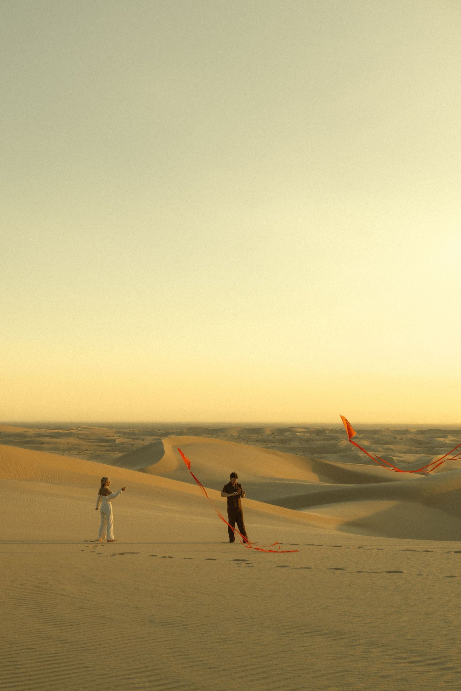Couple flying red kites on golden sand dunes at sunset in a vast desert landscape.