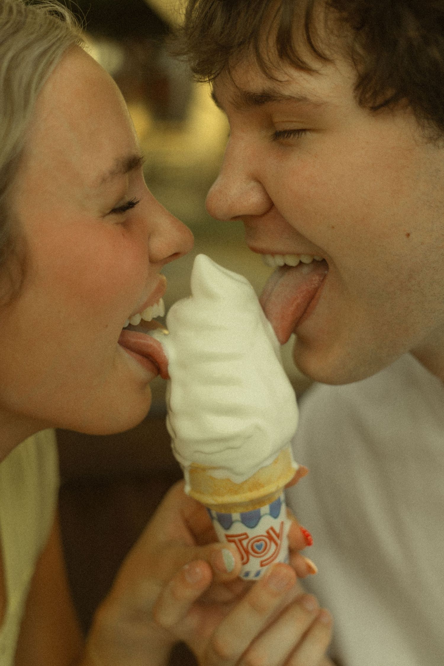 Smiling couple sharing a soft serve vanilla ice cream cone, licking it from both sides in a playful moment.