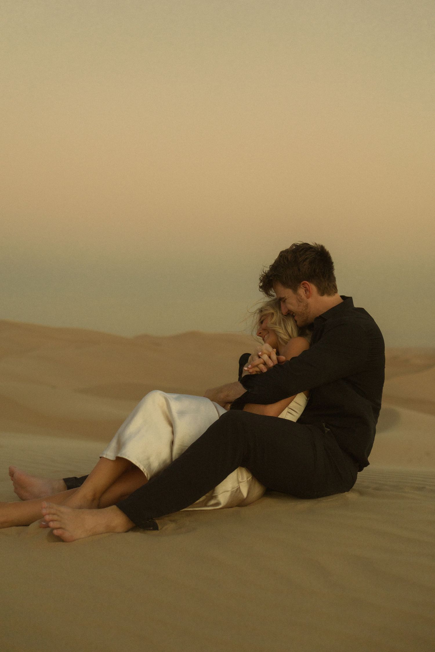 Couple sitting intimately together on desert sand dunes at golden hour sunset.