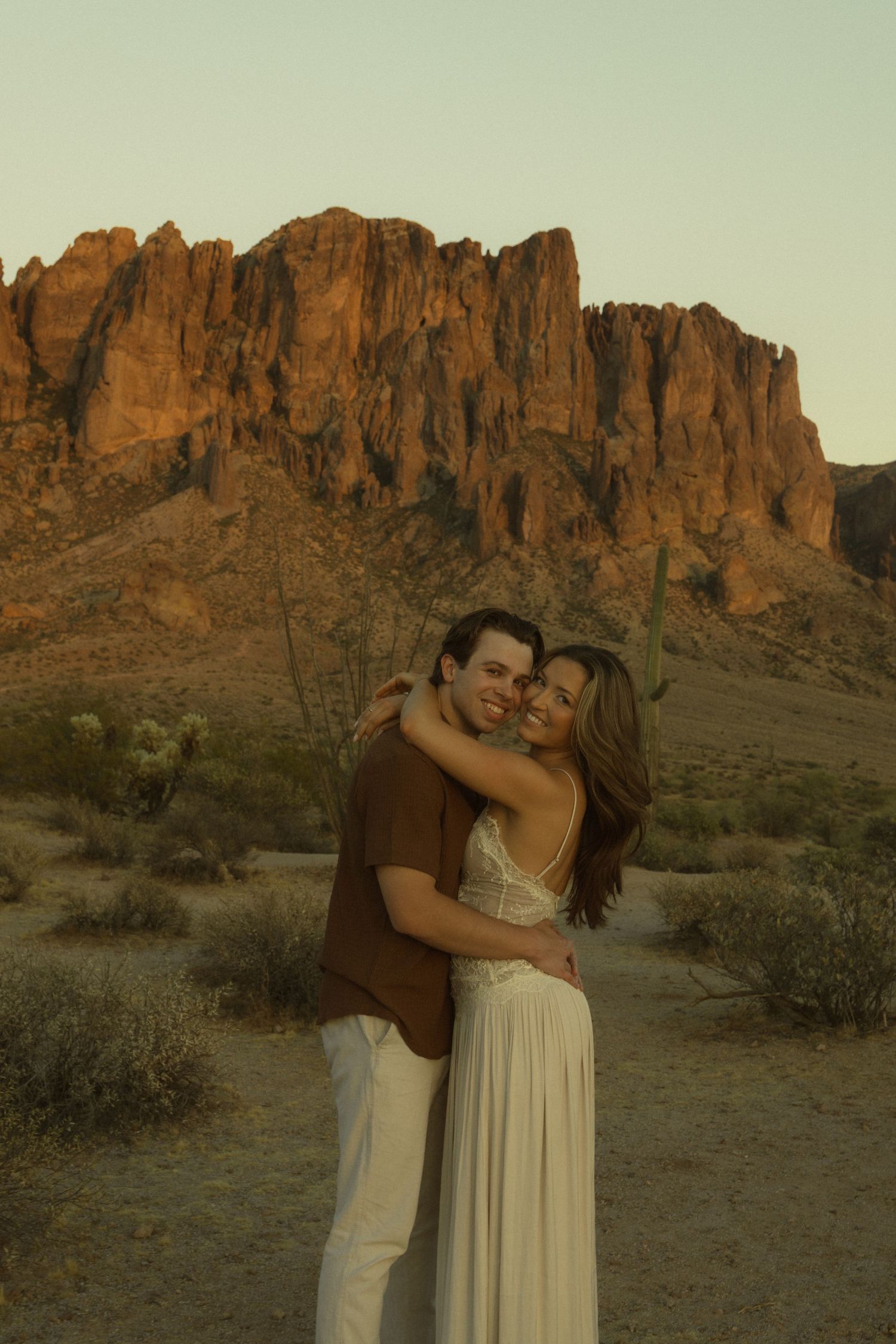 Couple embracing and smiling in Arizona desert with Superstition Mountains at golden hour.