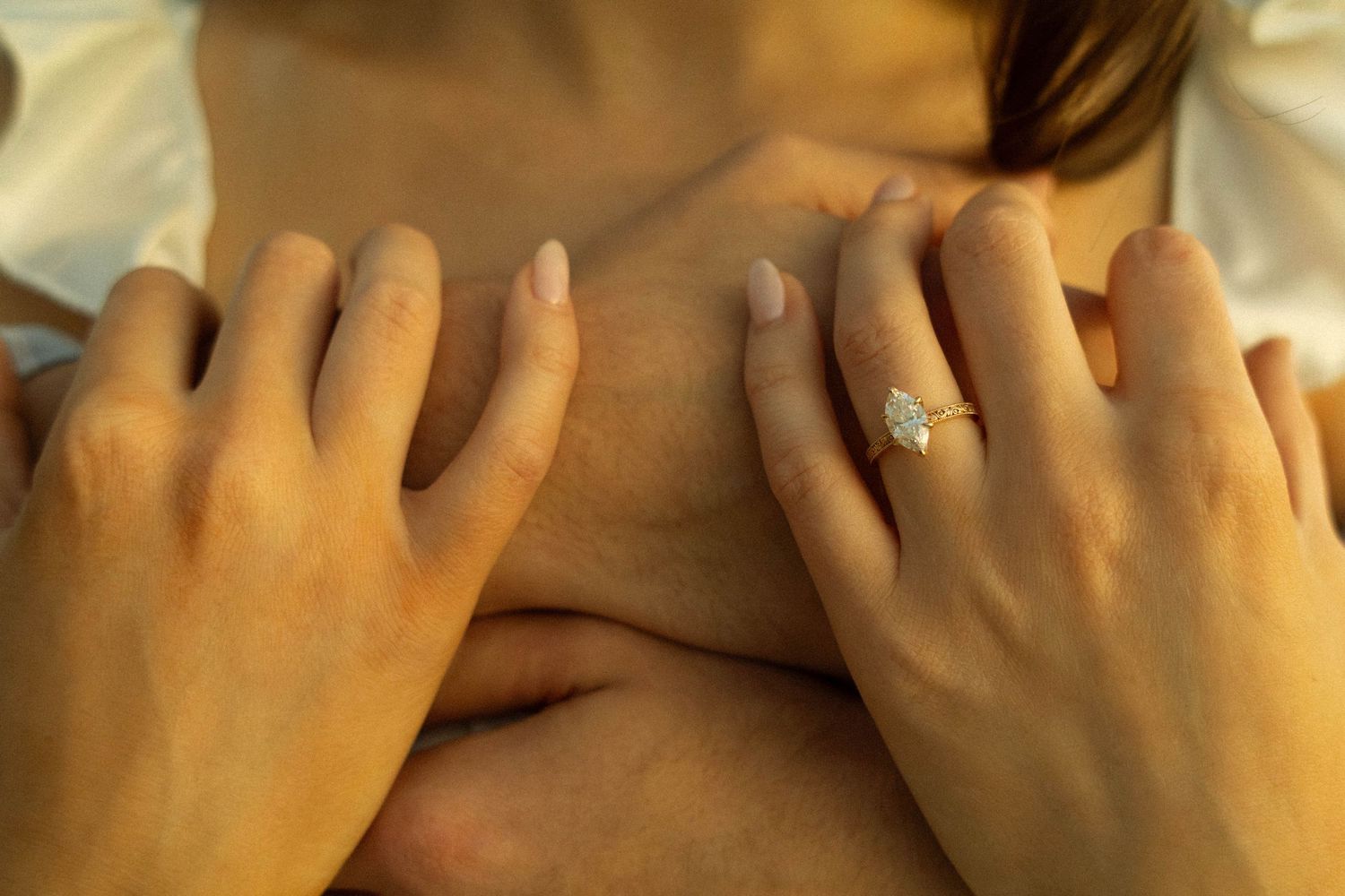 Close-up shot of hands with an engagement ring resting on natural wood texture.