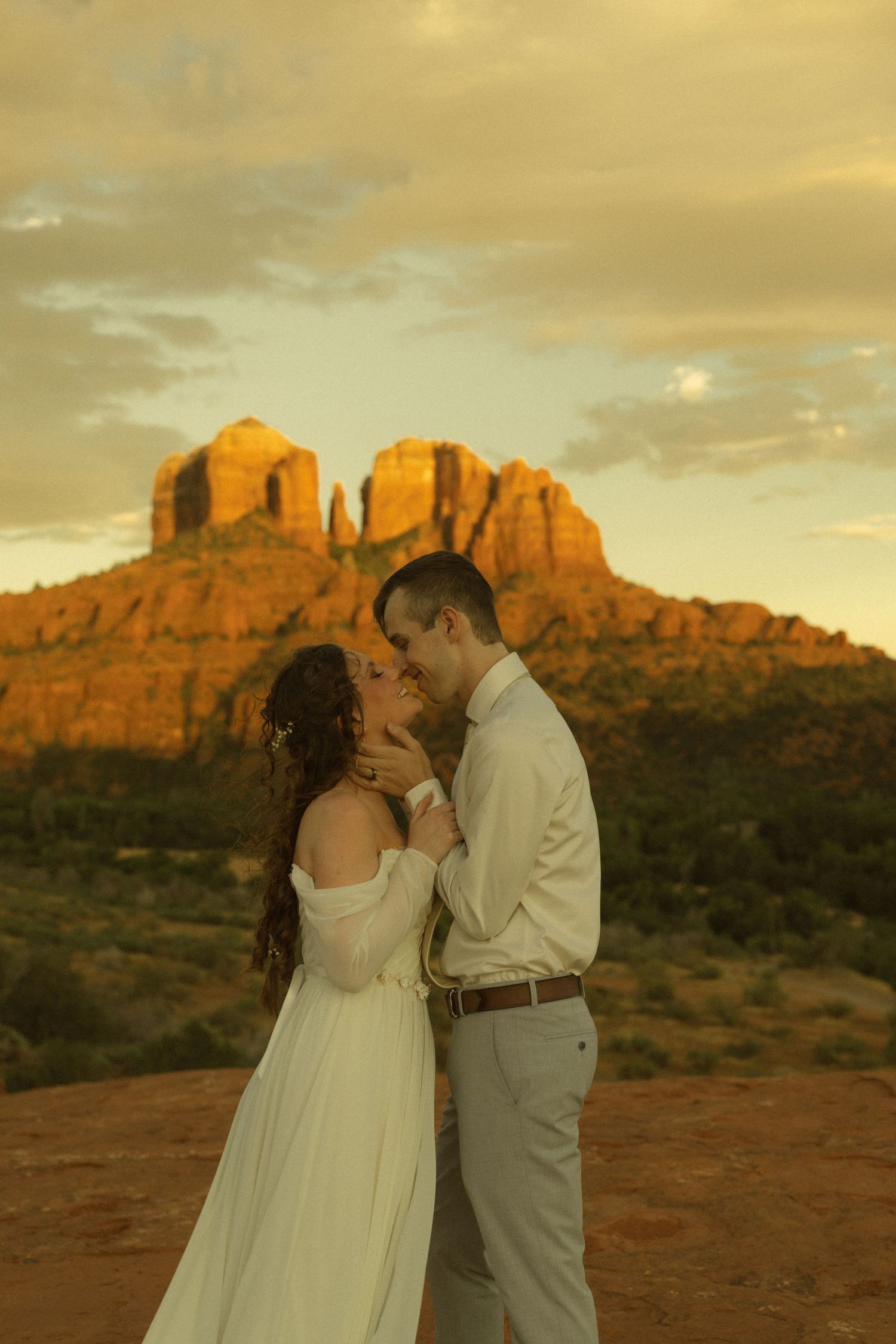 Couple shares romantic kiss at sunset with Cathedral Rock in Sedona, Arizona glowing golden in the background.