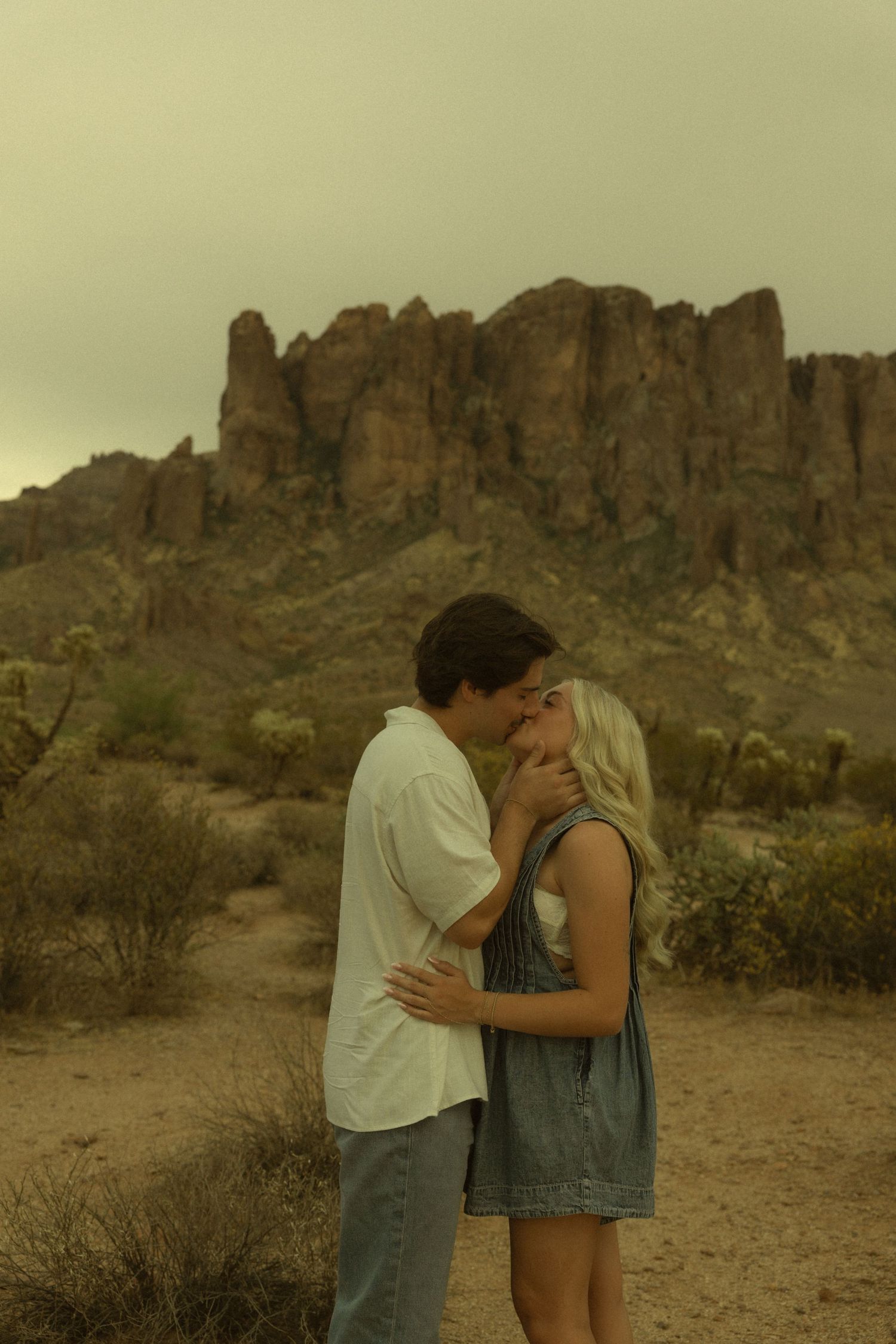 Couple sharing a romantic kiss in the Arizona desert with rugged Superstition Mountains backdrop.