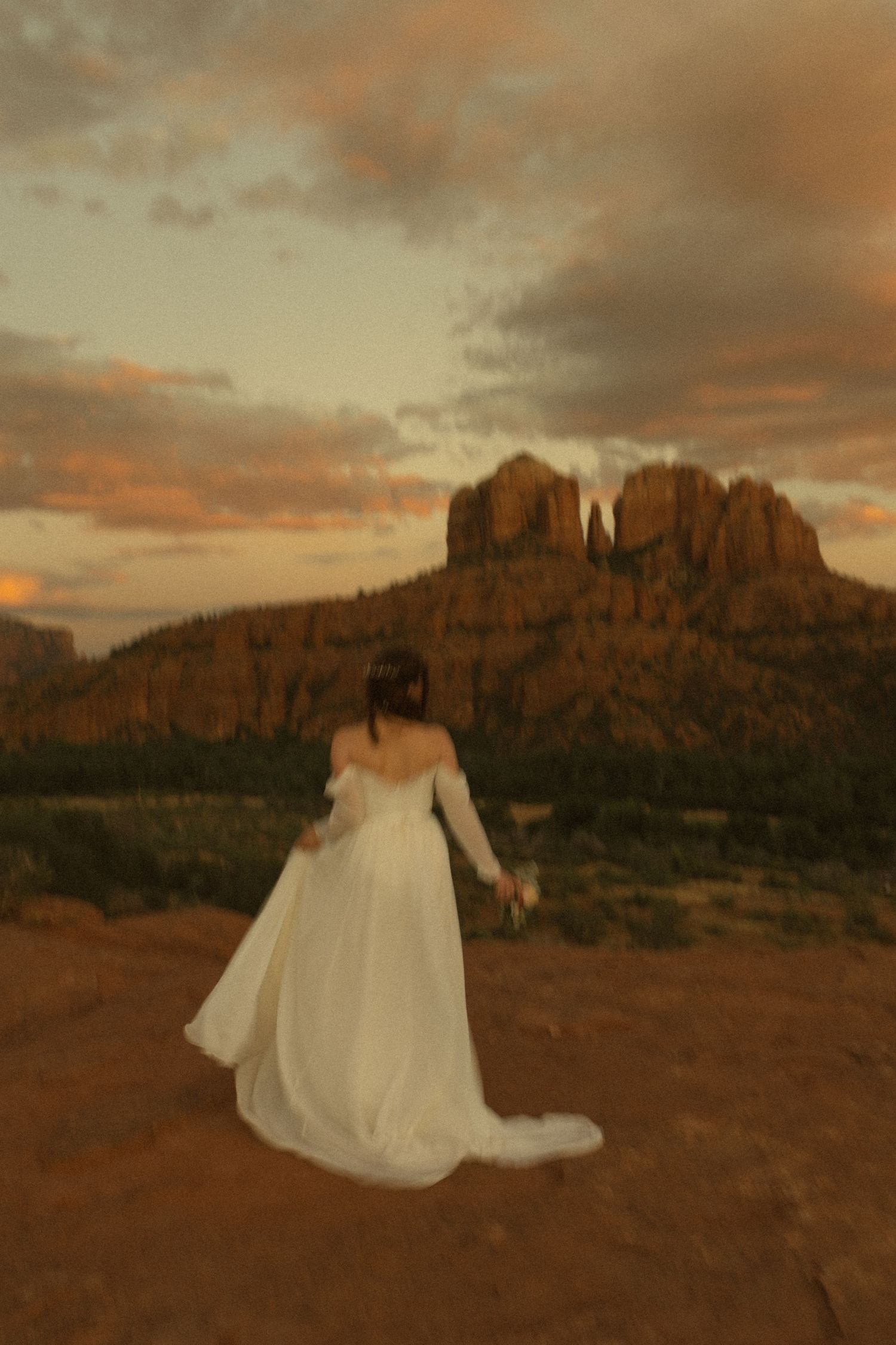 Bride in white gown stands before Cathedral Rock at sunset in Sedona, Arizona, red rocks glowing golden.