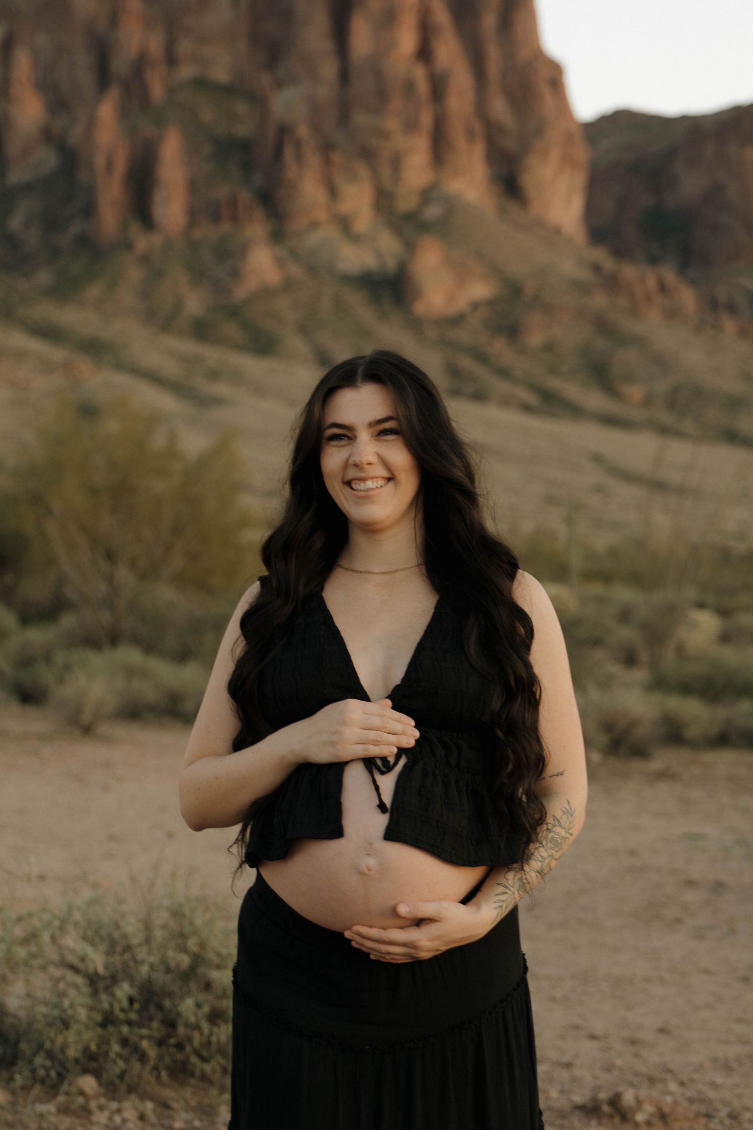 A maternity photo session in front of rugged desert cliffs at sunset with dramatic lighting and natural scenery.