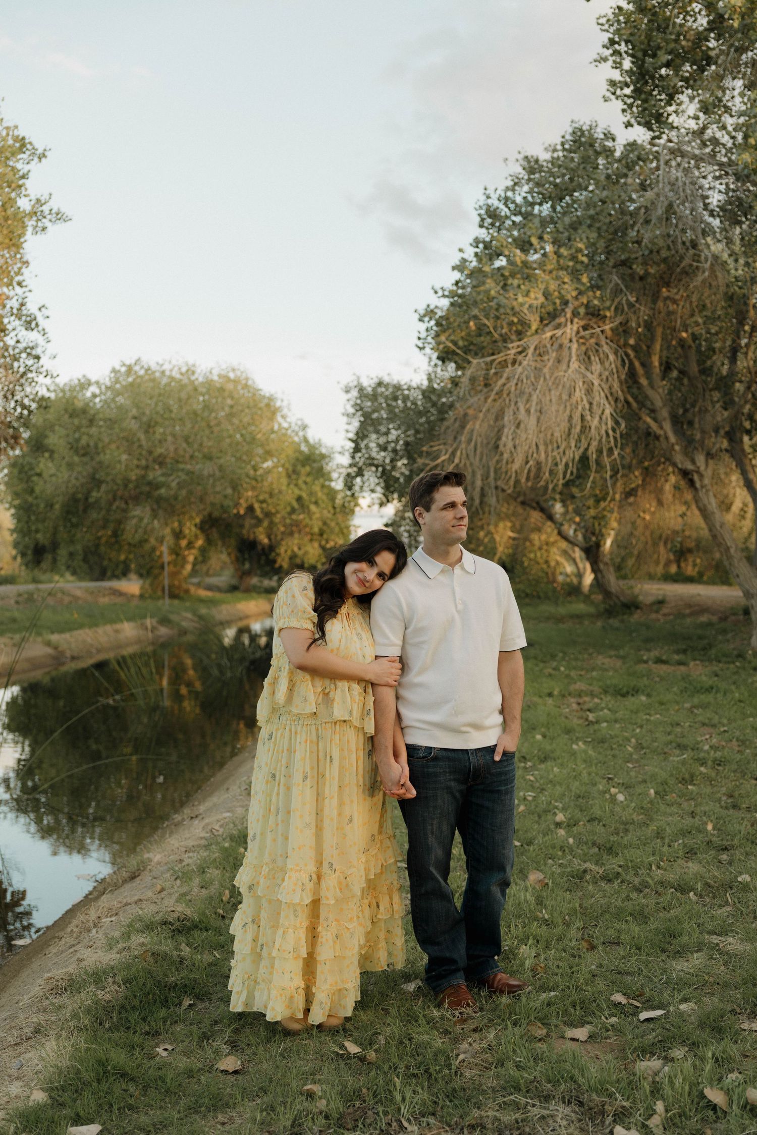 A couple shares a tender moment by a pond in a serene natural setting during golden hour.