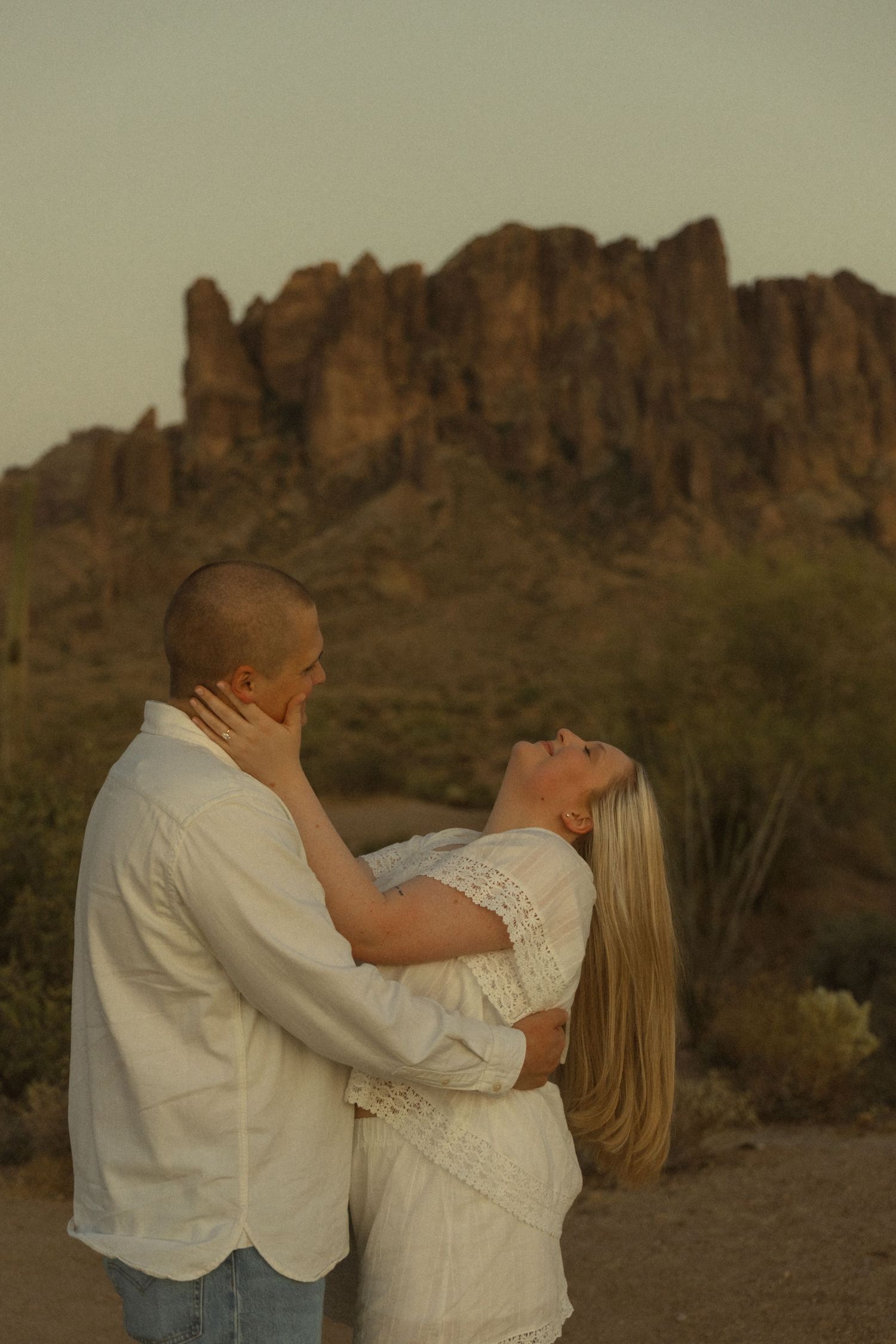 Romantic couple embracing at sunset with Superstition Mountains desert landscape in the background.