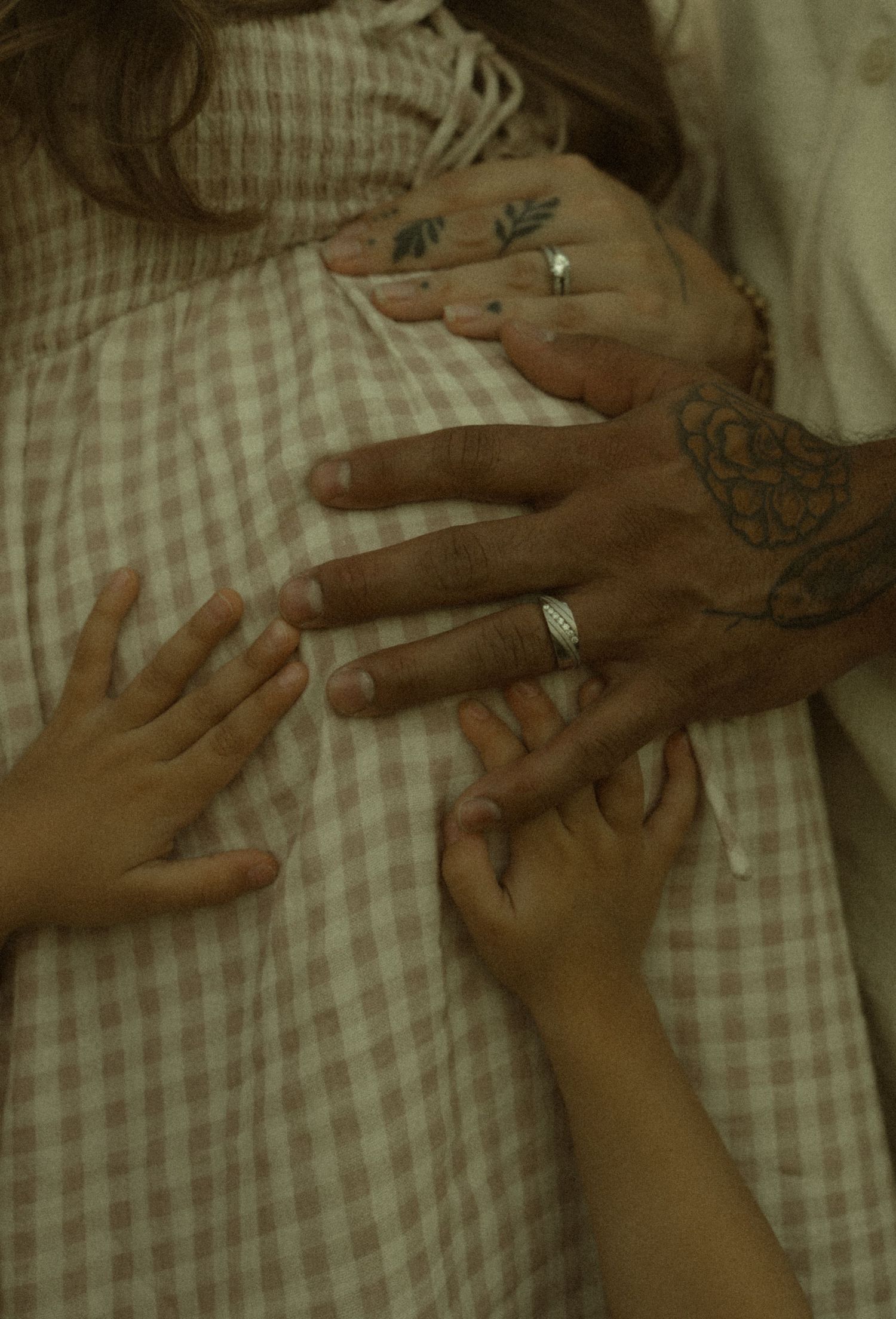 Close-up of family hands resting on pregnant woman's belly, showing tattoos and rings.