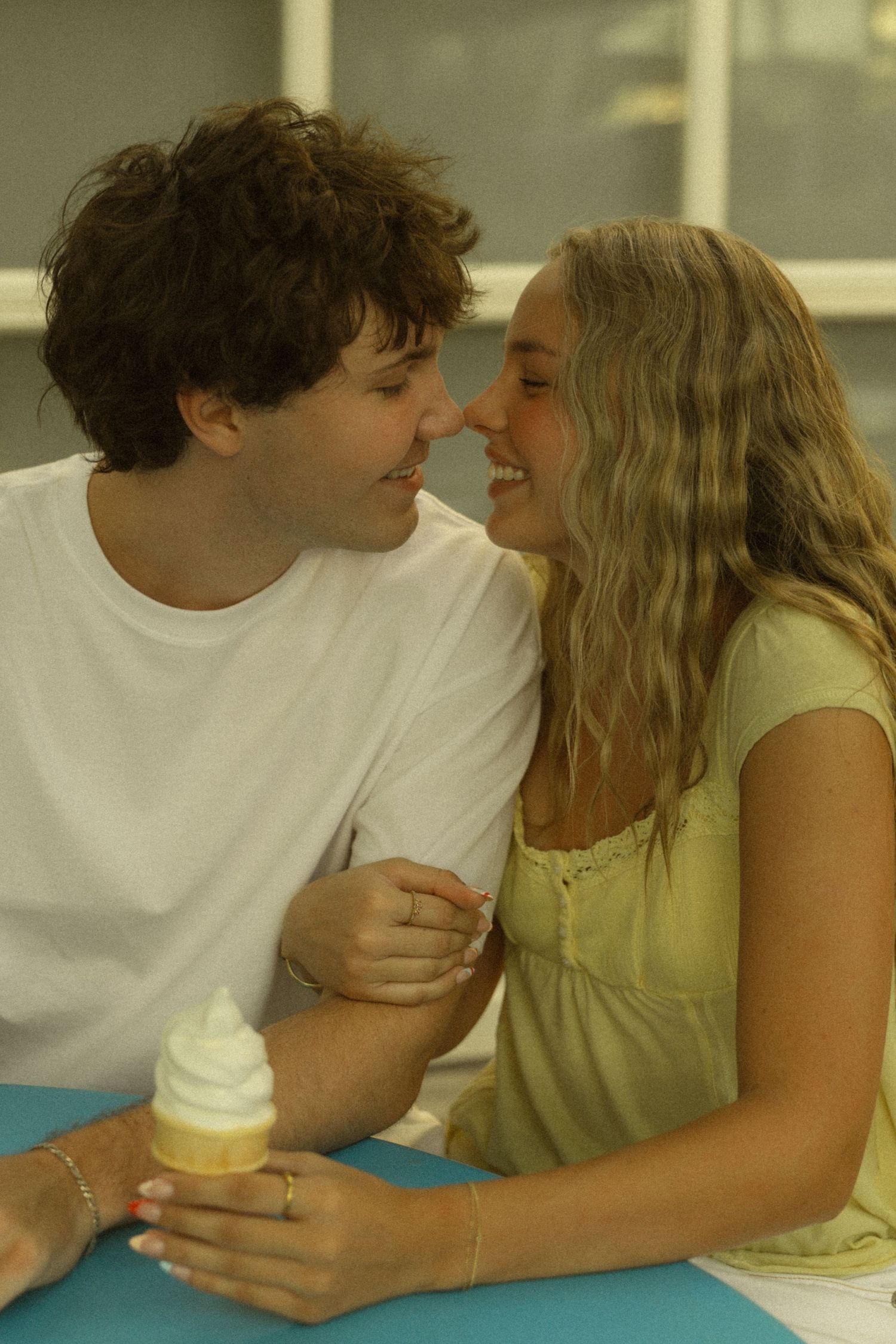 Young couple sharing a soft serve ice cream cone, smiling and leaning close together at a turquoise table.