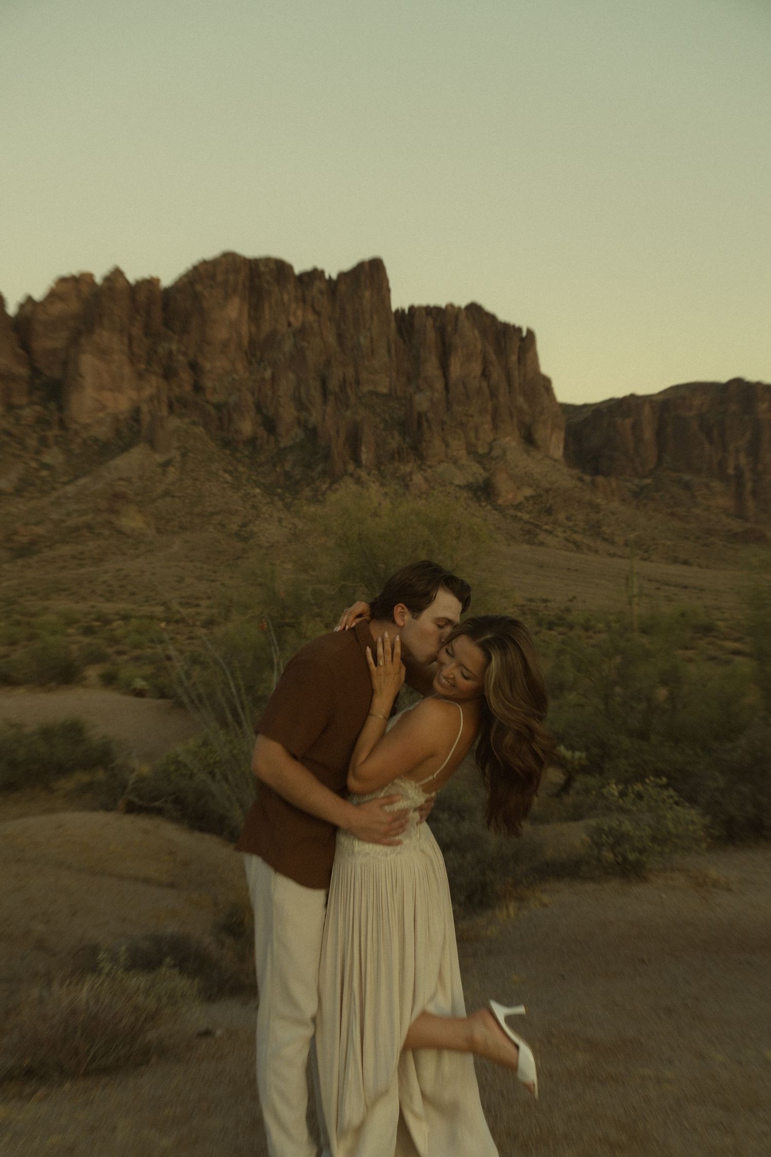 Couple embracing at sunset with Superstition Mountains in the Arizona desert background.