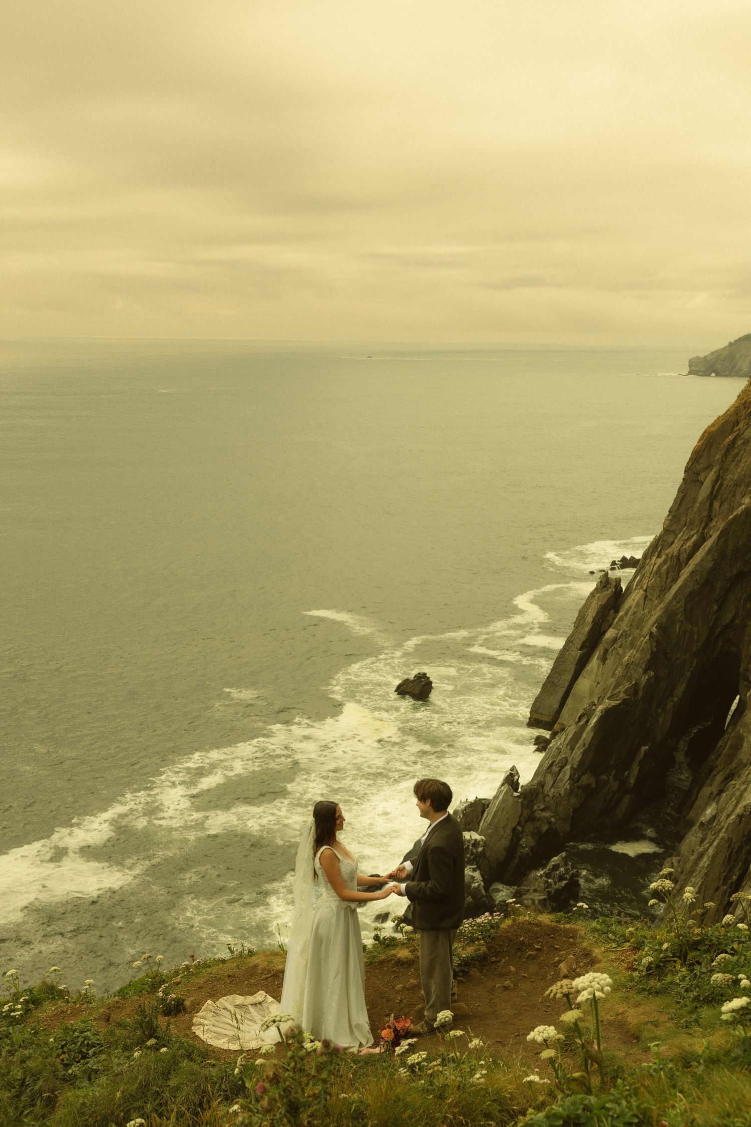 Couple exchanging vows on a dramatic coastal cliff overlooking the ocean on their wedding day.