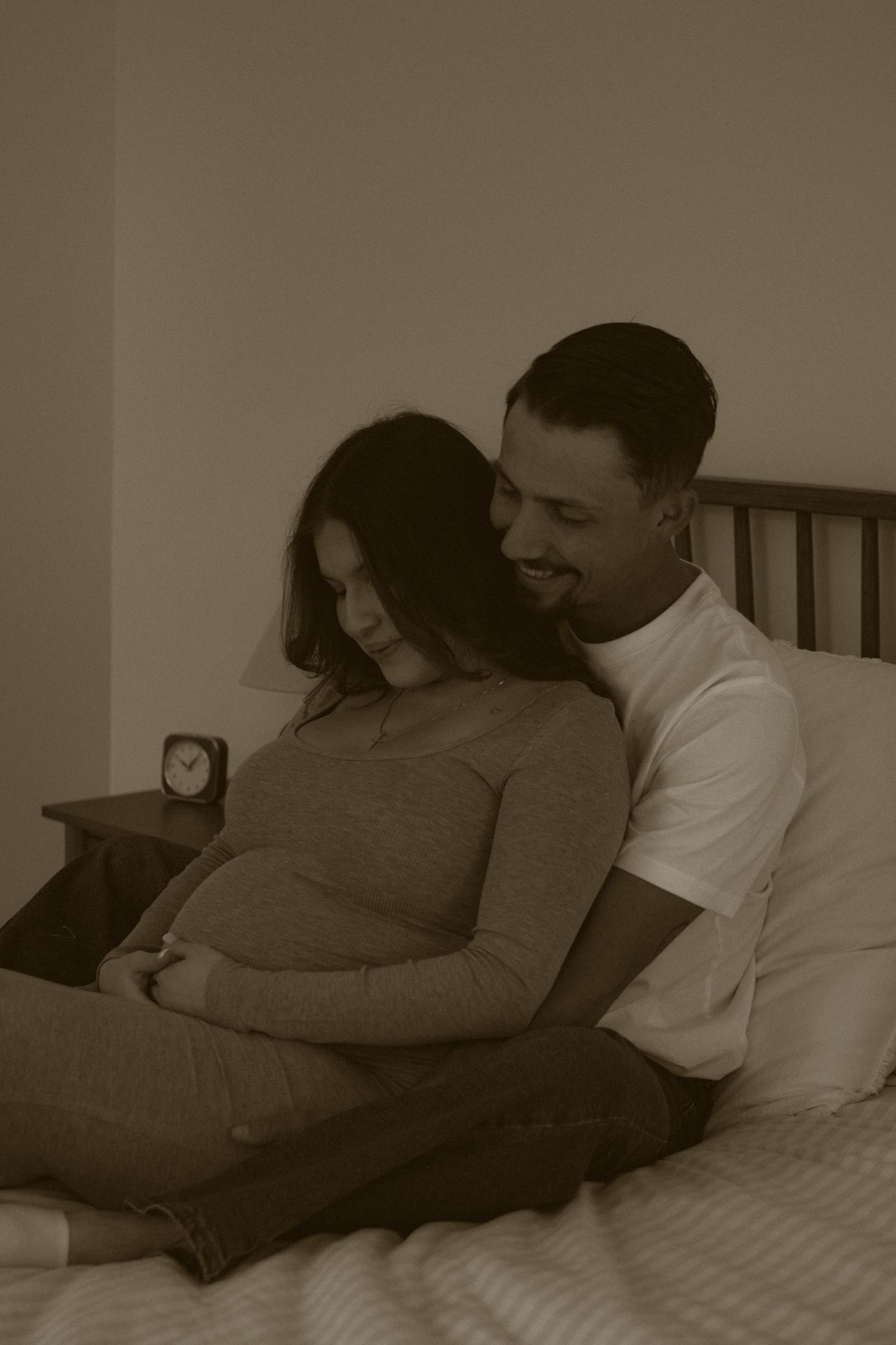 A tender moment captured in sepia tones showing comfort and connection between two people on a bed.