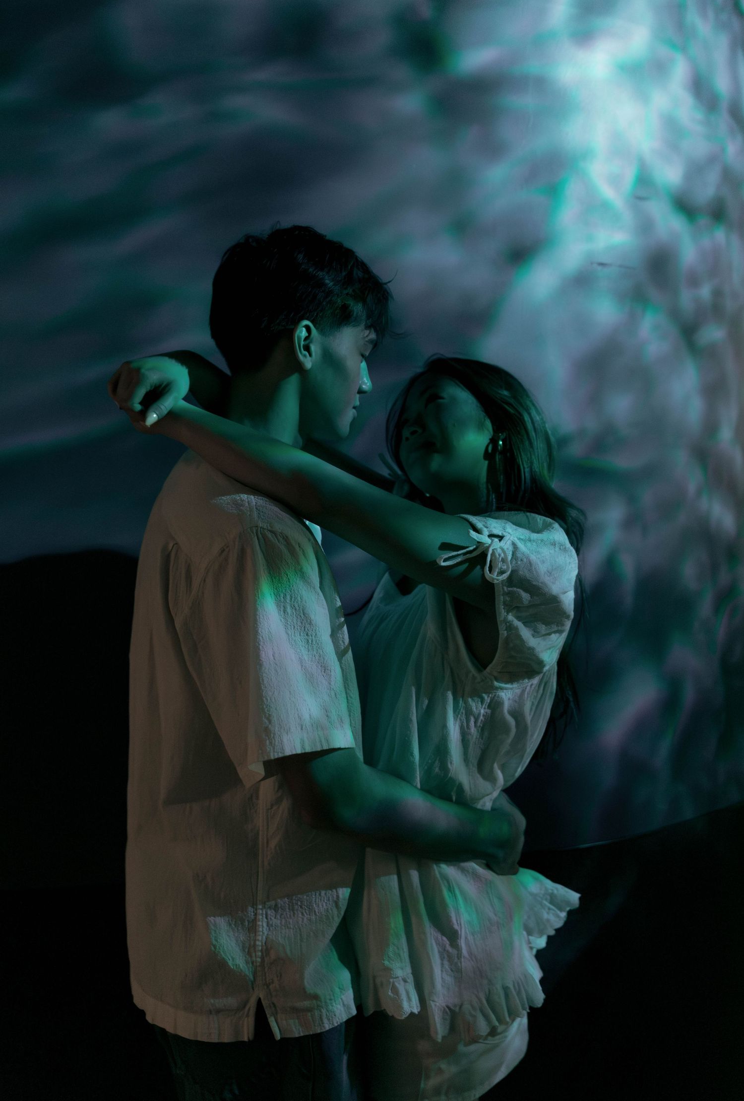 Couple embracing in front of an ethereal aquarium backdrop with turquoise lighting.