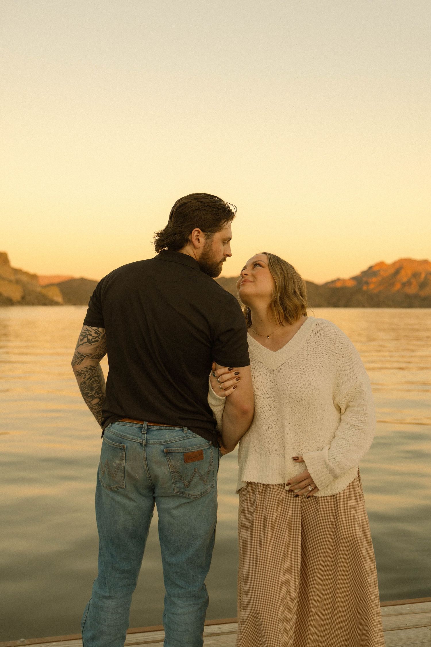A couple stands together at sunset by the water's edge in a romantic seaside moment.