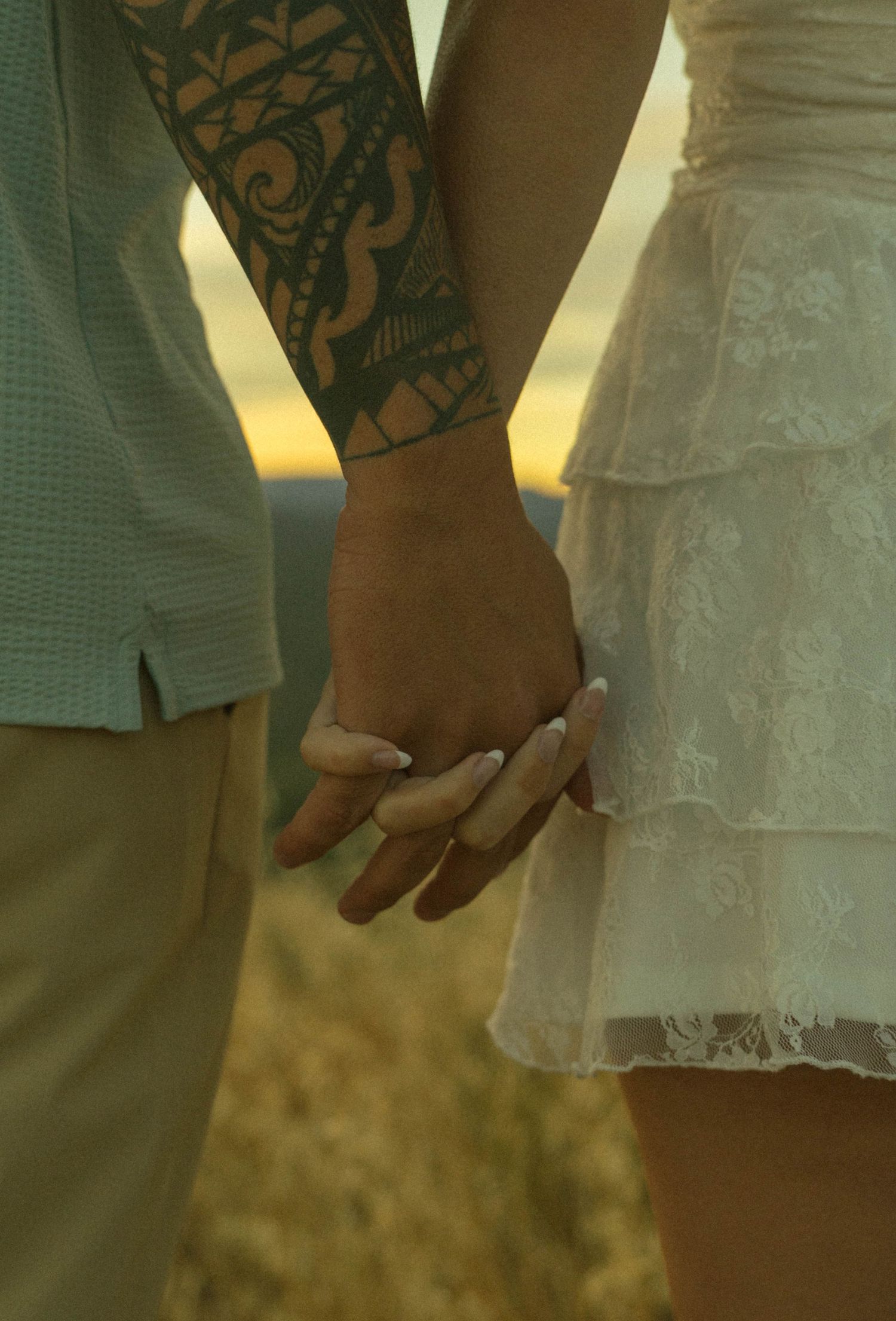 Close-up of couple holding hands showing tribal tattoo and white lace dress.