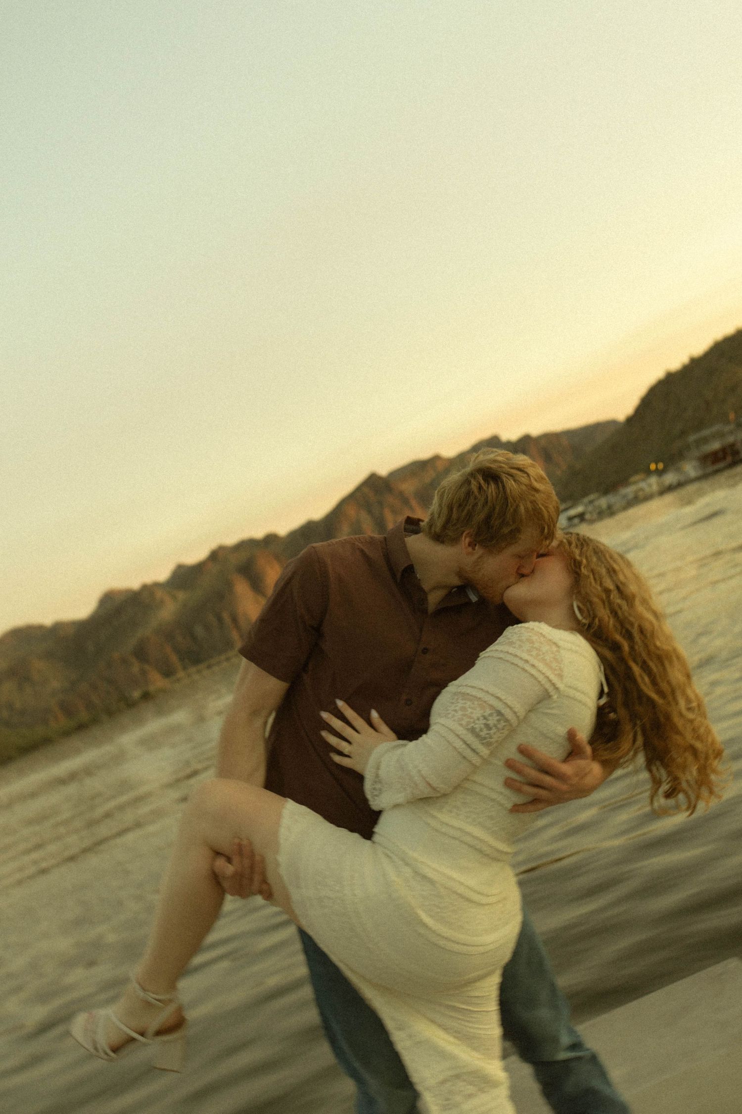 Romantic dance dip pose between couple against scenic waterfront landscape at dusk.