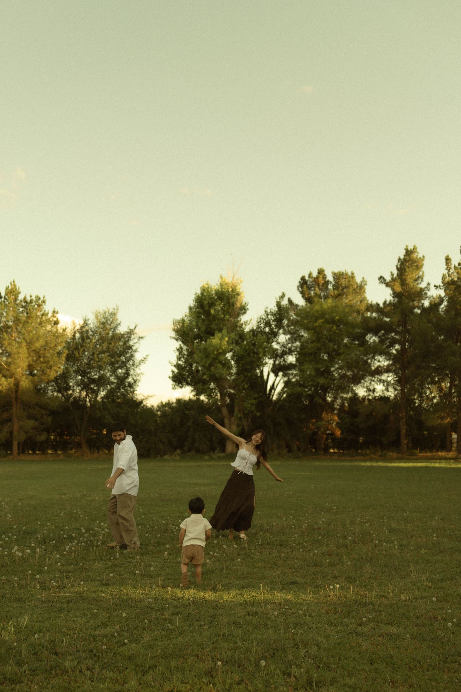 Woman twirling joyfully with family in a sunlit green park at golden hour.