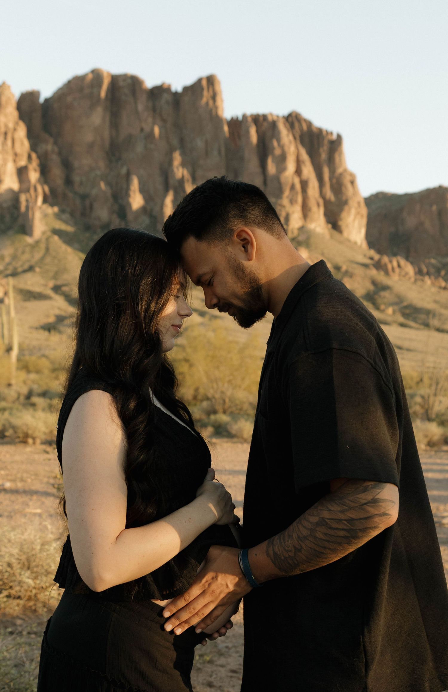 A couple dressed in black shares romantic moments against a desert mountain landscape.
