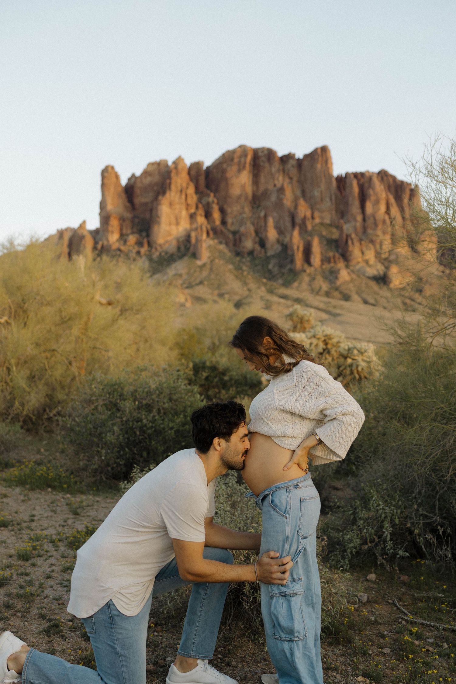 A couple embraces during a maternity photo session with dramatic desert rock formations in the background.