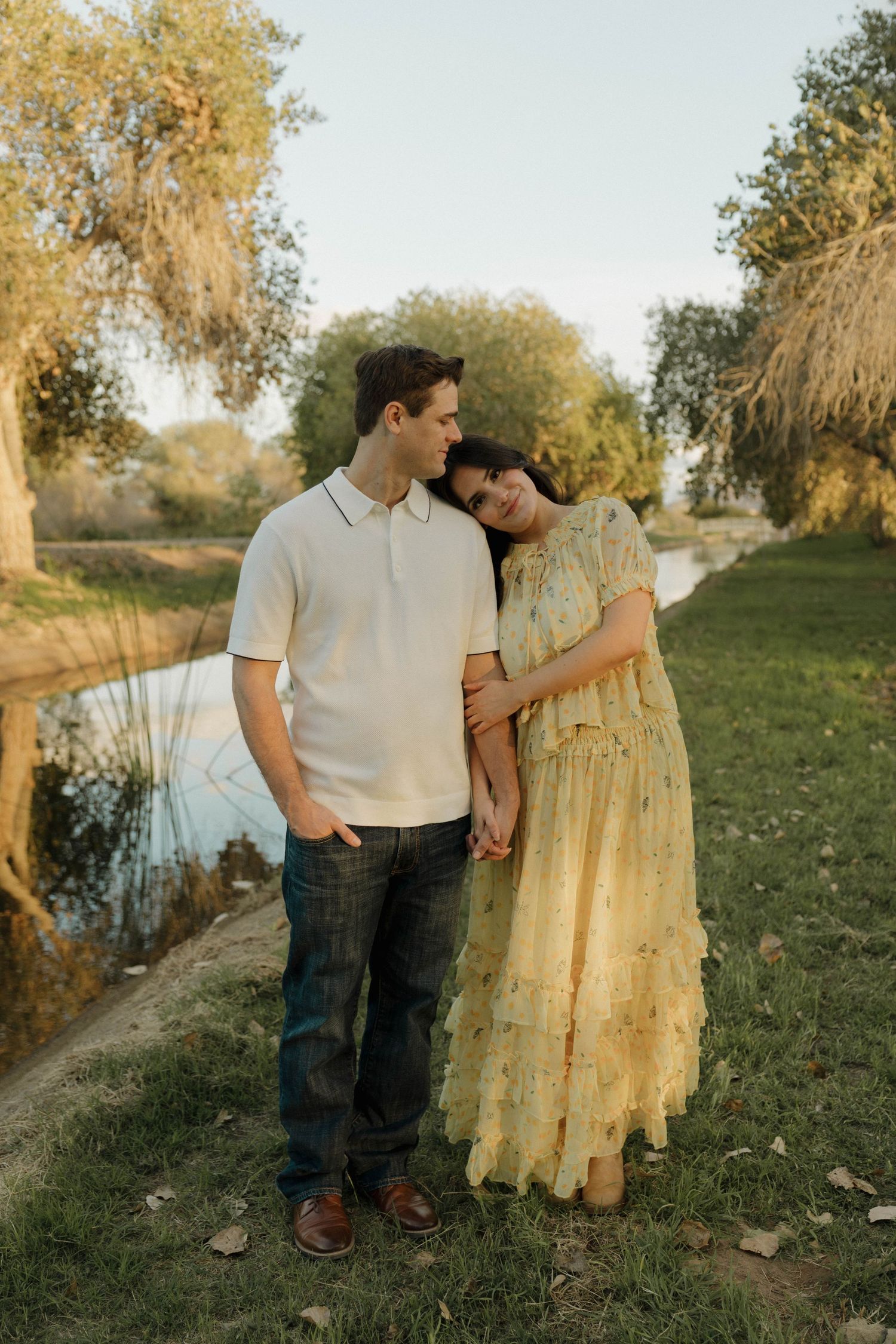 A couple shares romantic moments by a rustic wooden fence in a sunlit meadow during golden hour.