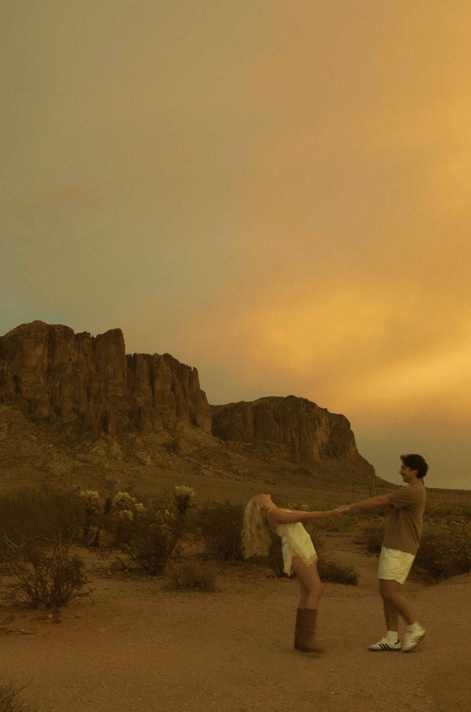 Couple dancing at sunset in the desert with dramatic orange sky and rocky Superstition Mountains backdrop.