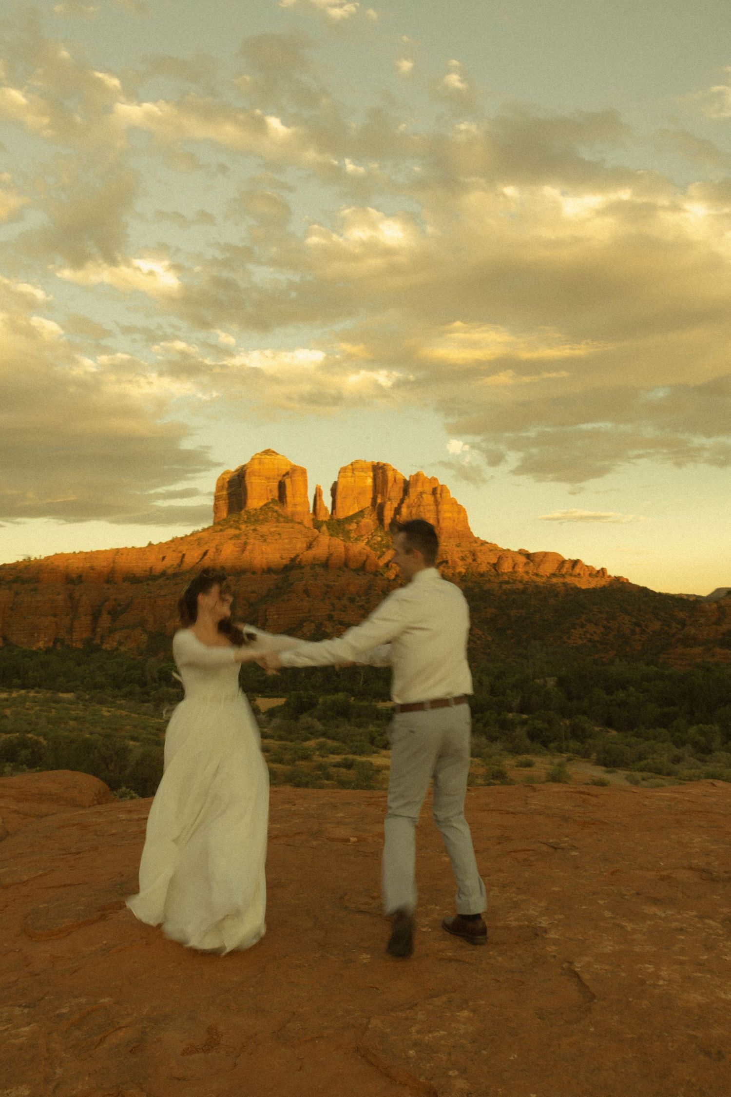Couple dancing at sunset in front of Cathedral Rock in Sedona, Arizona, with golden clouds overhead.