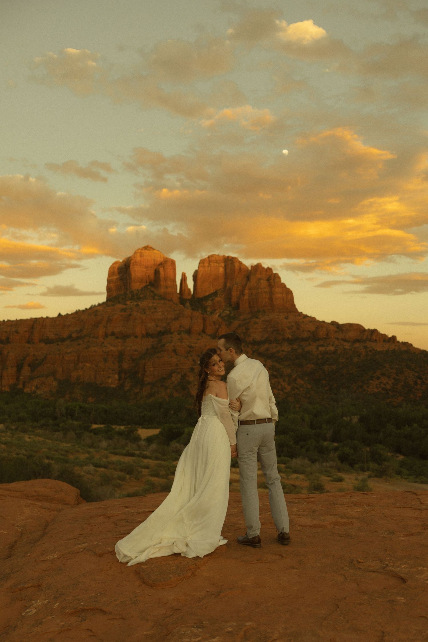 Couple sharing a kiss in wedding attire at sunset with Cathedral Rock in Sedona, Arizona glowing golden in the background.