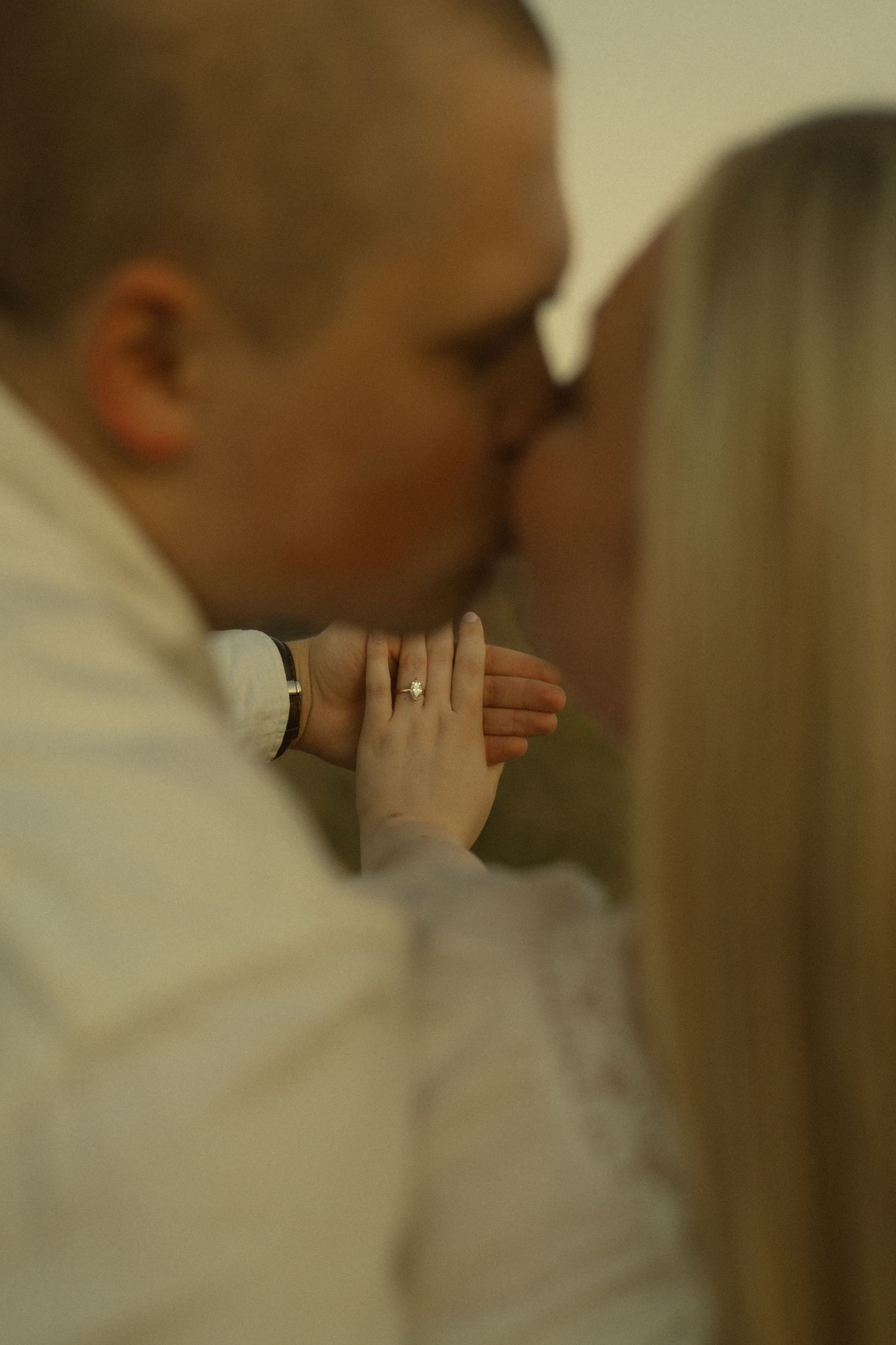 Couple sharing a kiss while showcasing an engagement ring, captured in an intimate close-up portrait.