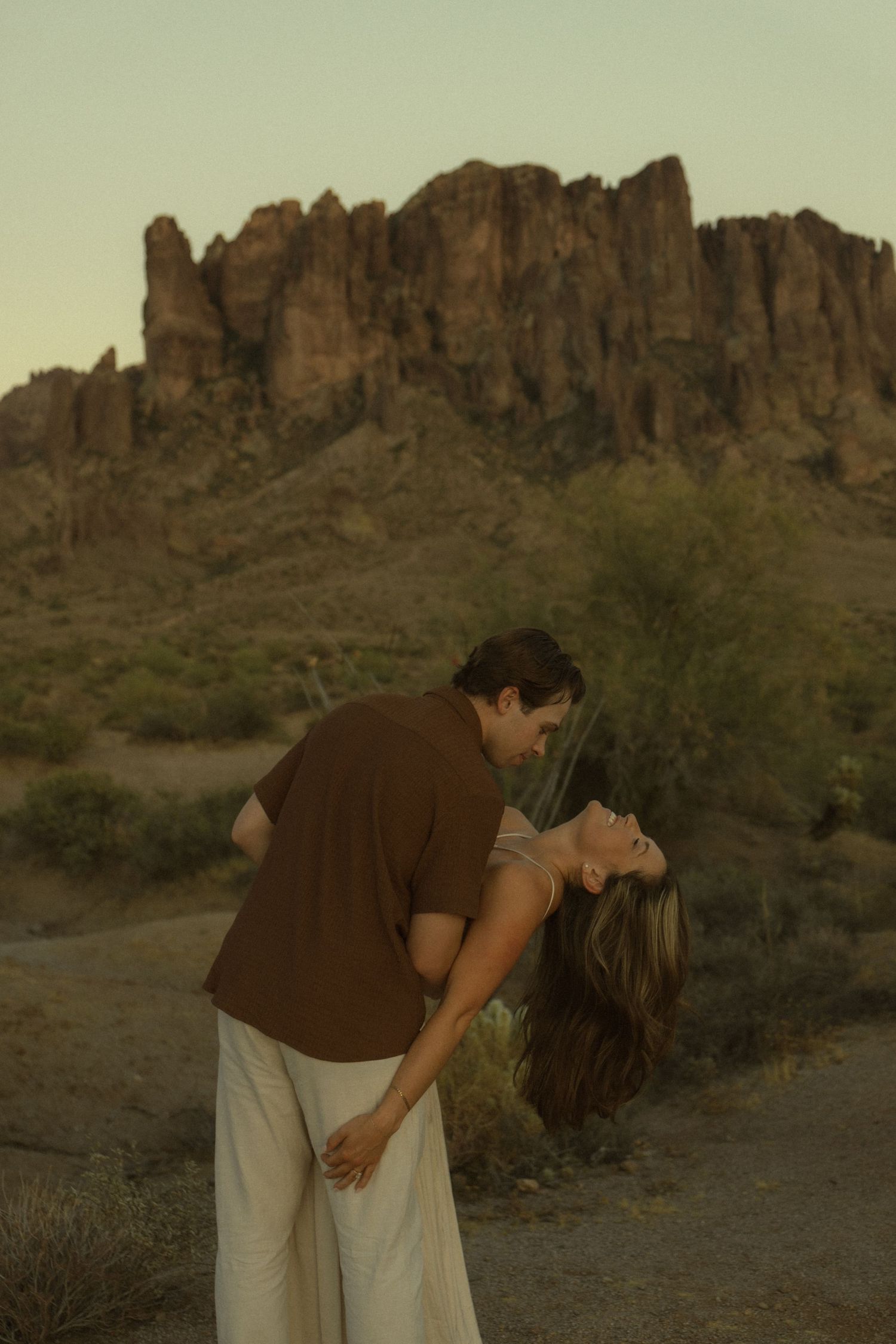 Couple sharing a romantic dip pose in the Arizona desert with Superstition Mountains at golden hour.