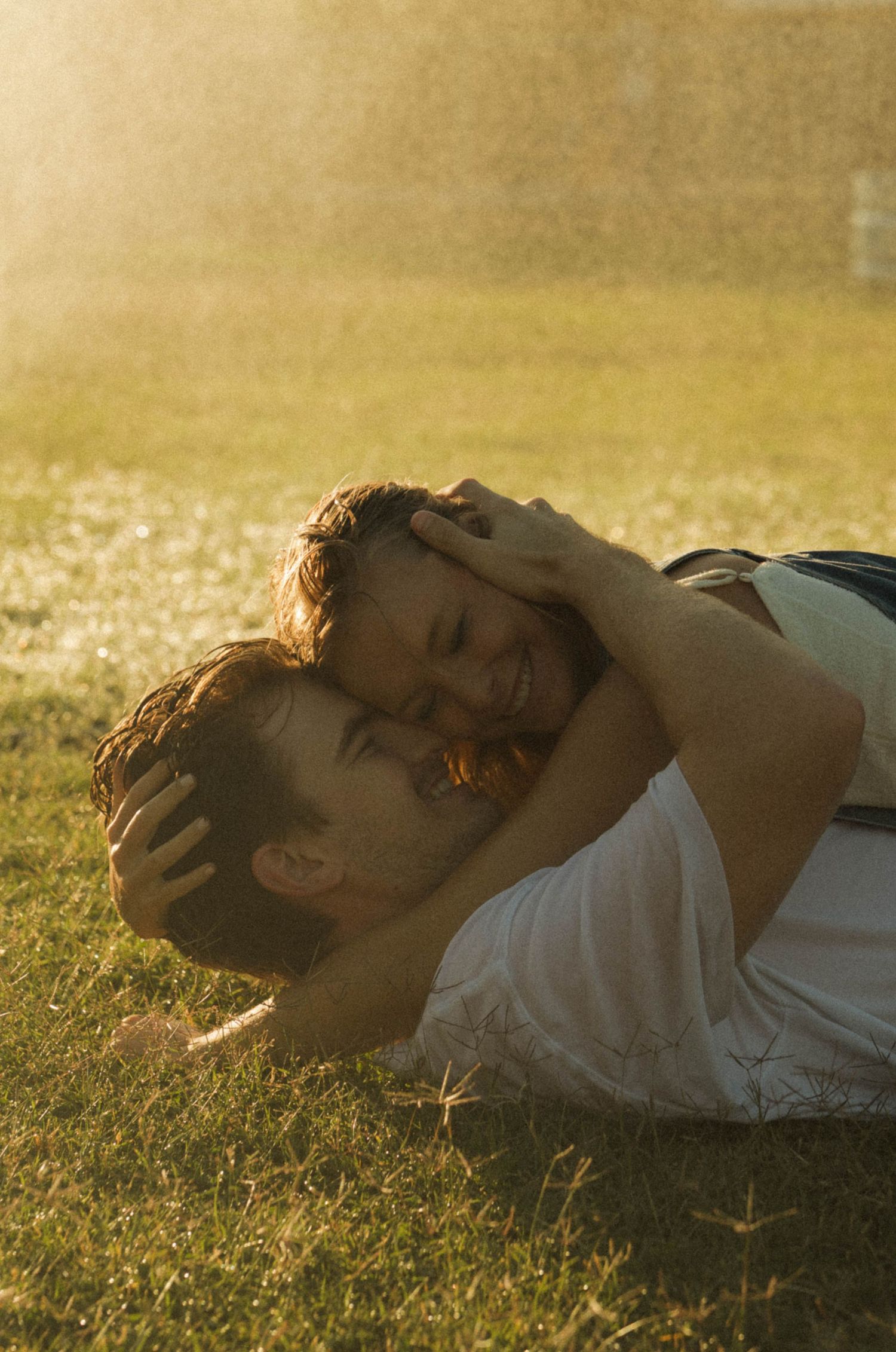 Couple embracing on green grass in golden sunlight, sharing a romantic moment outdoors.