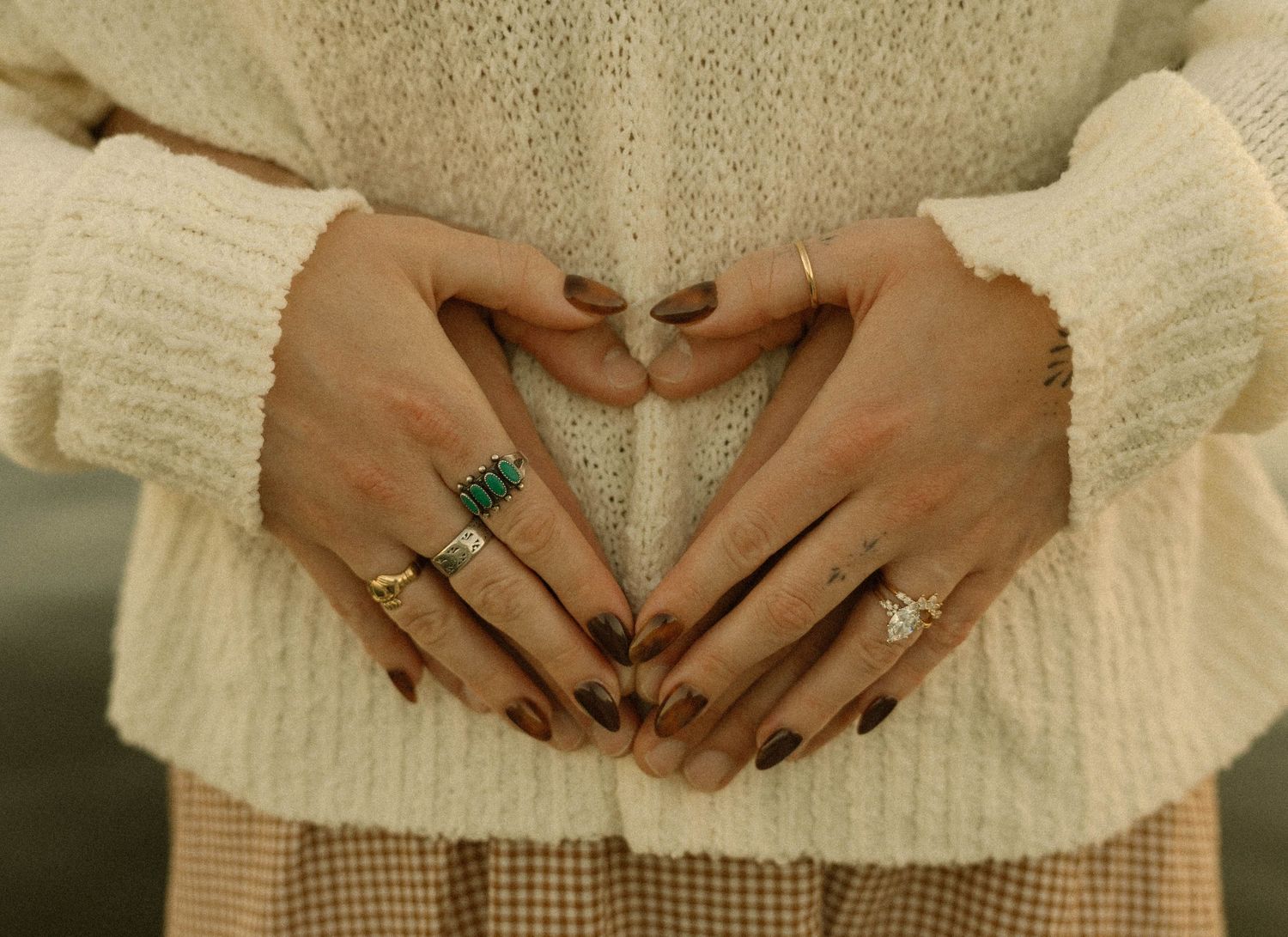 A series of hands making heart shapes against a cream colored sweater background.