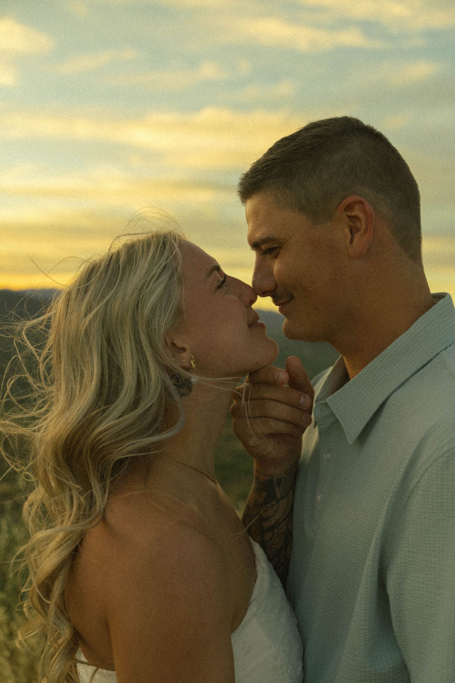 Couple sharing a romantic moment at golden hour sunset, smiling and almost kissing outdoors.