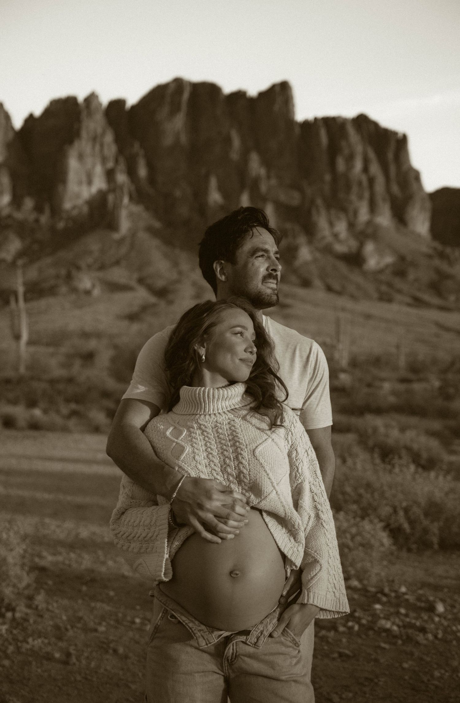 Sepia-toned maternity portraits with dramatic desert mountain backdrop and intimate couple poses.