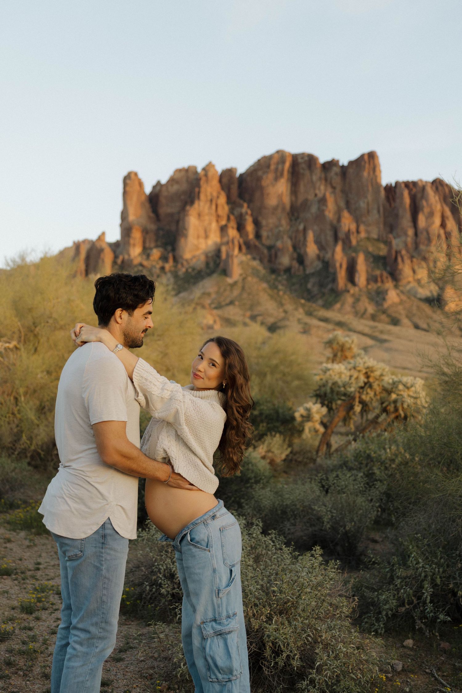 Romantic desert photoshoot with dramatic mountain cliffs and desert vegetation in the background.