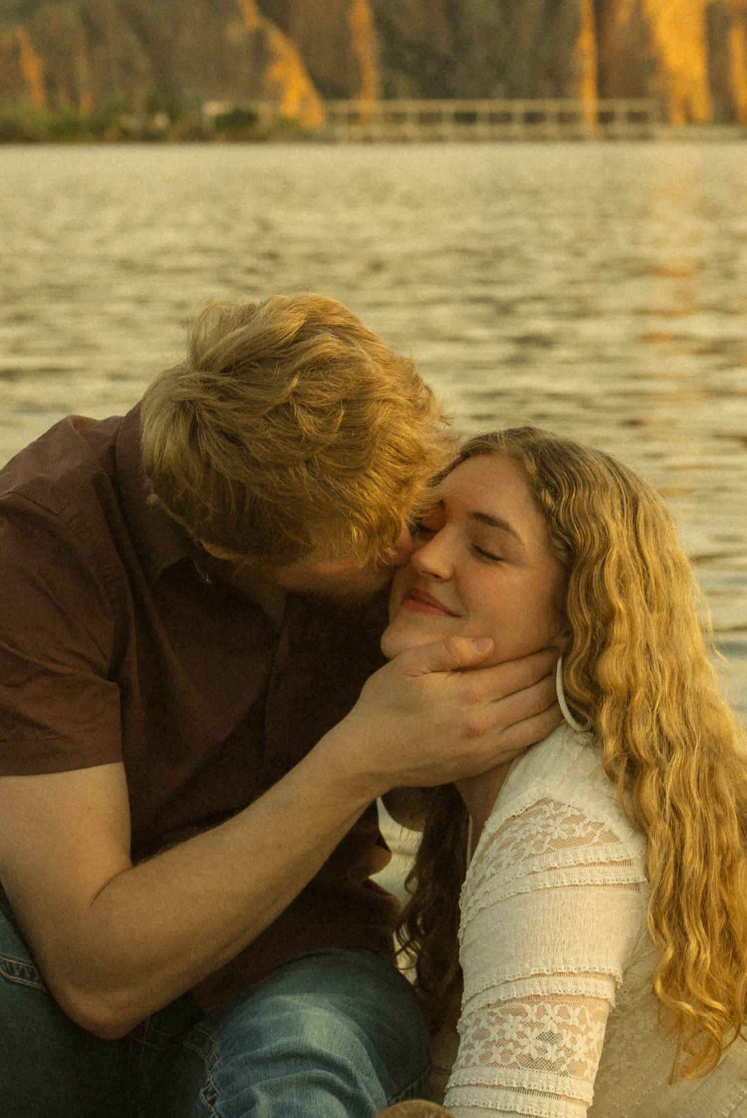 A romantic couple shares an intimate moment by the water during golden hour.