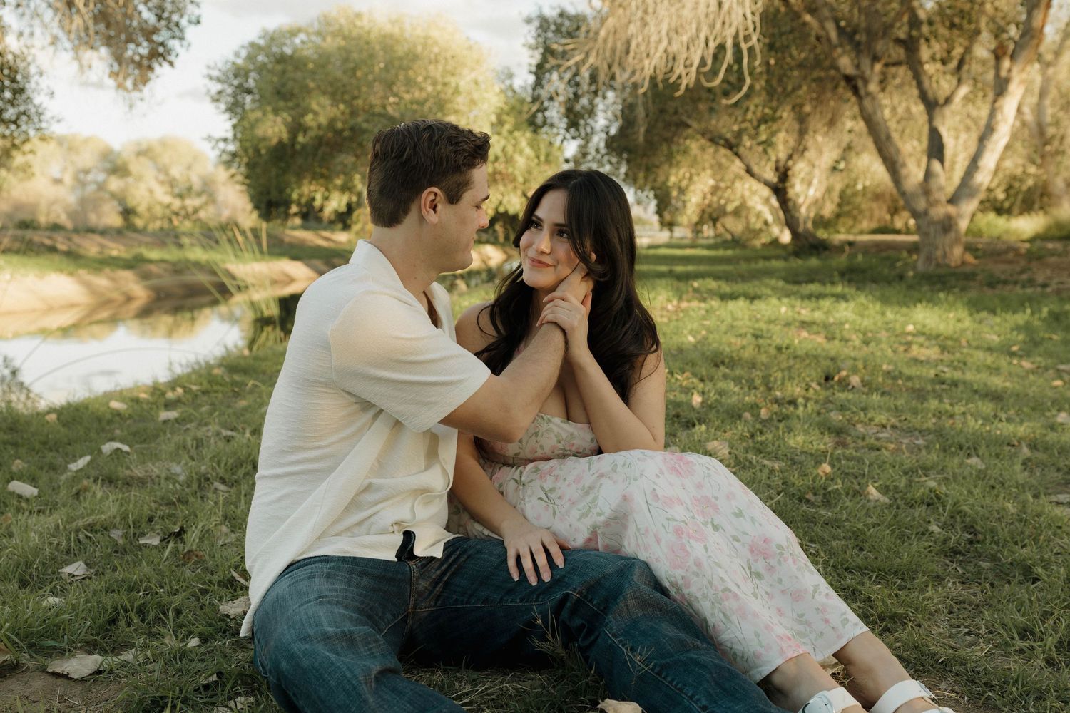 Couple shares romantic moments in a sunlit meadow near a pond during golden hour.