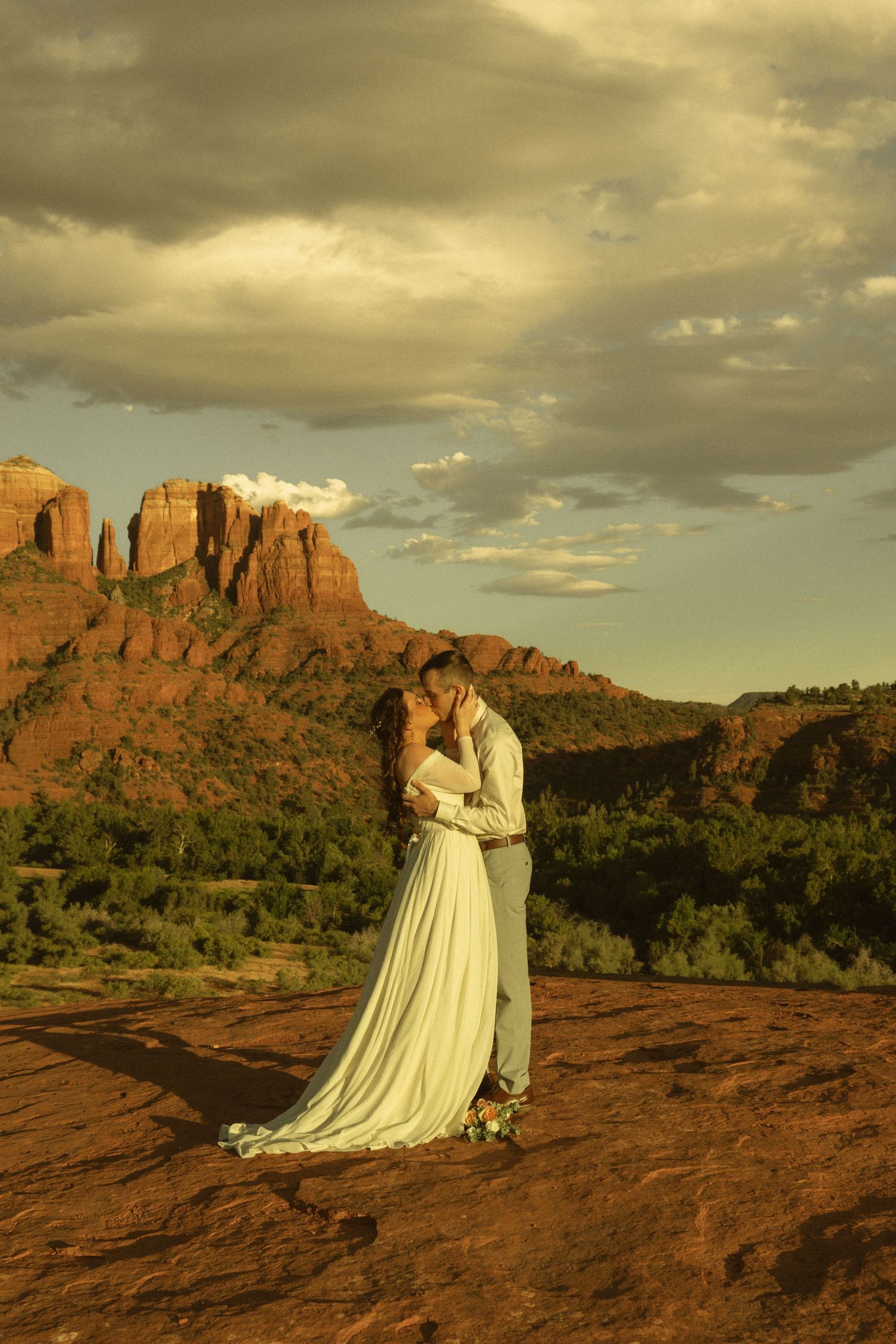 Couple sharing a romantic kiss in wedding attire against Sedona red rock formations at golden hour.