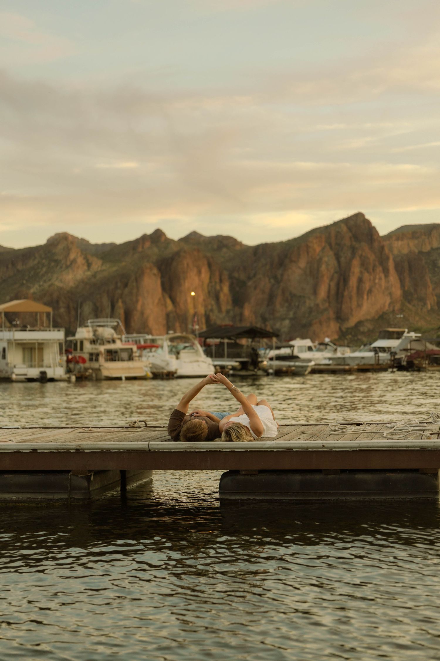 A scenic view of boats docked at a marina with rugged mountains and warm sunset colors.