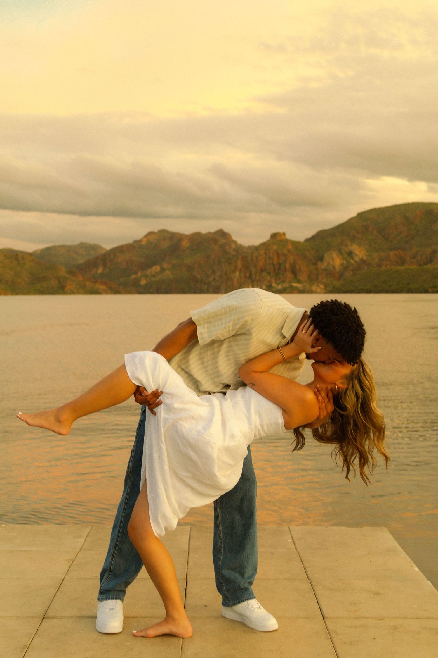 A romantic dance pose at sunset with mountains and water in the background on a stone platform.