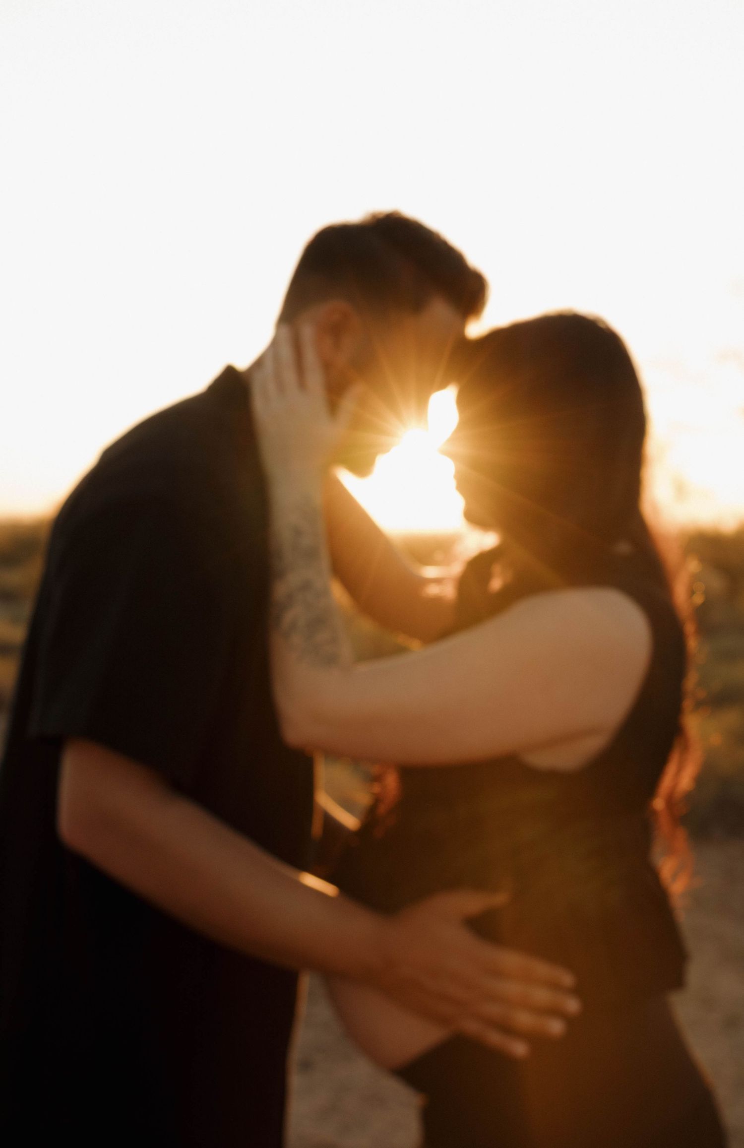 Romantic couple sharing an intimate moment against a golden sunset backdrop.