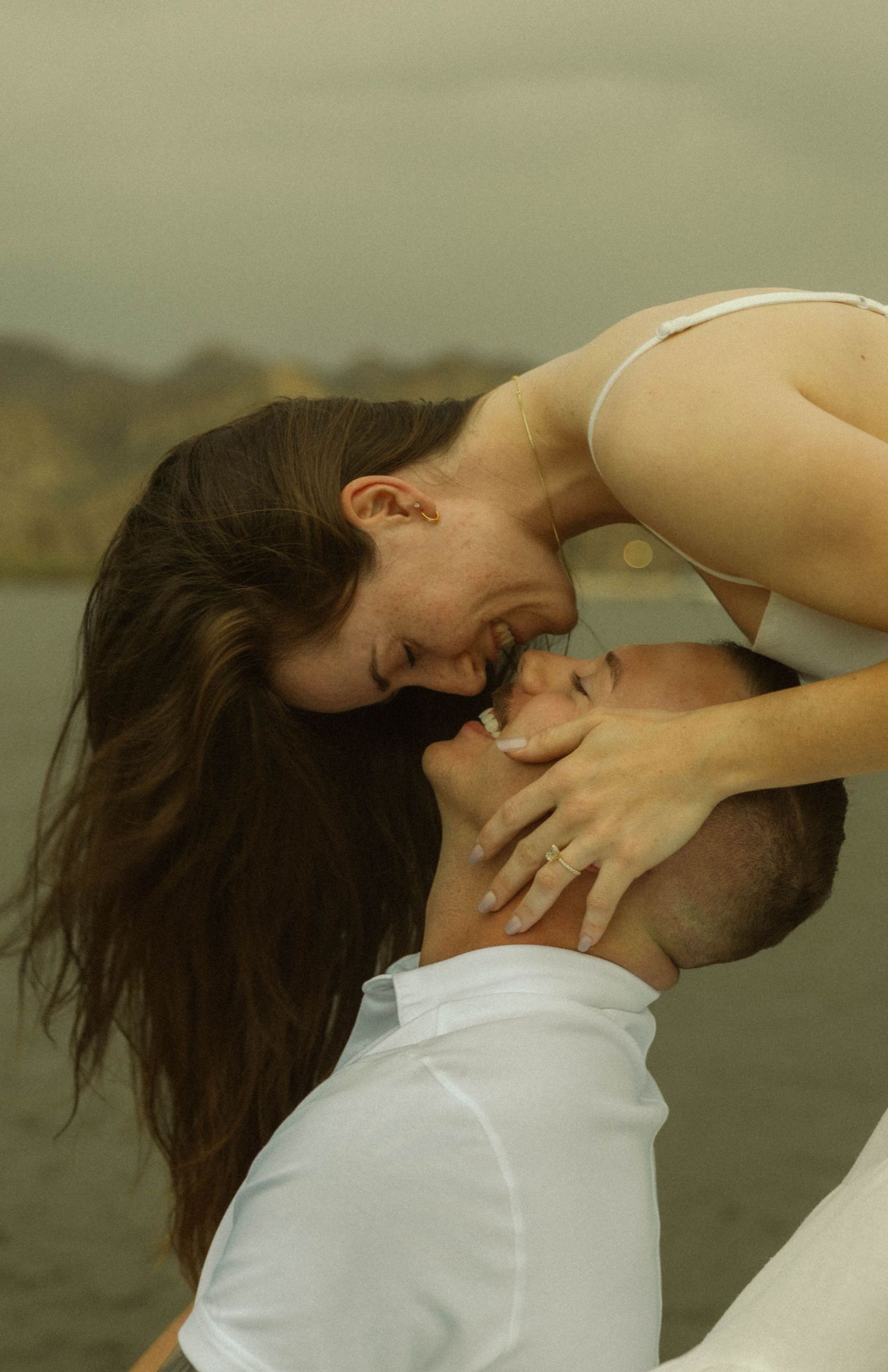 Intimate couple sharing a passionate moment against a moody coastal landscape.