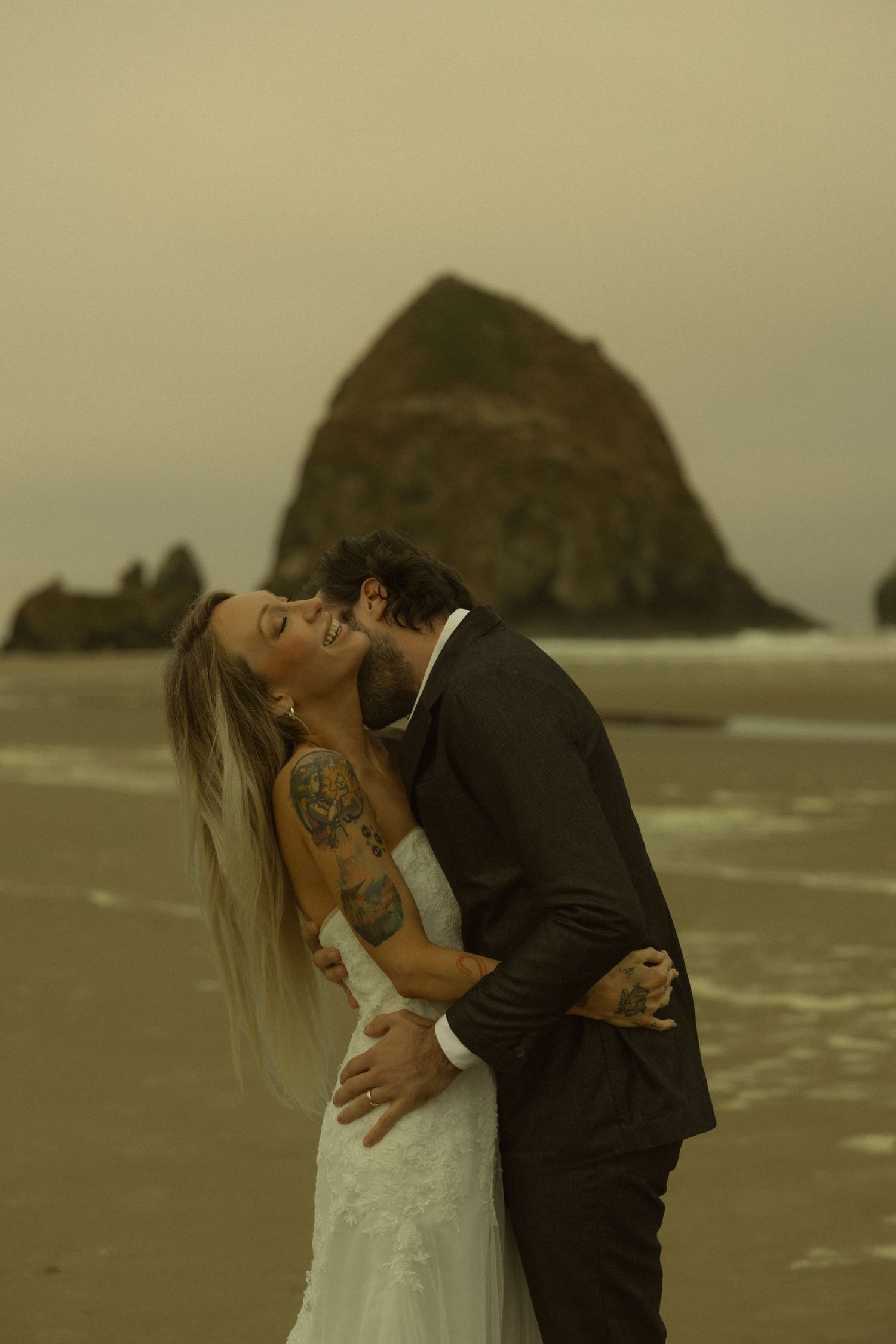 Bride and groom share a romantic kiss on the beach with Haystack Rock in the background at Cannon Beach.