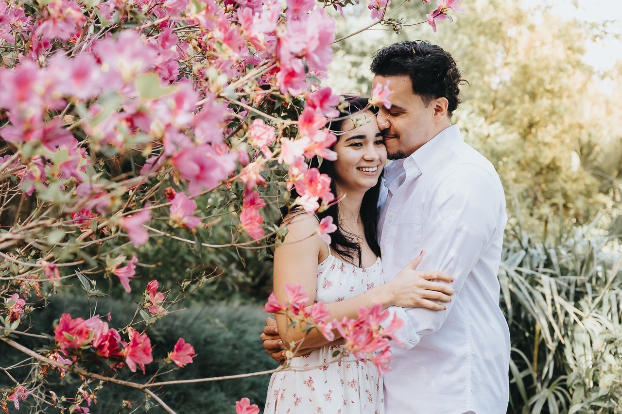 A romantic moment captured among blooming pink bougainvillea flowers in a sunlit garden setting.
