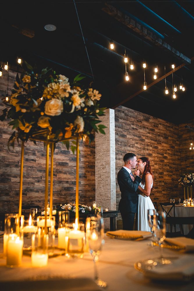 A romantic wedding reception venue with exposed brick walls, candlelight and hanging Edison bulbs creating intimate ambiance.