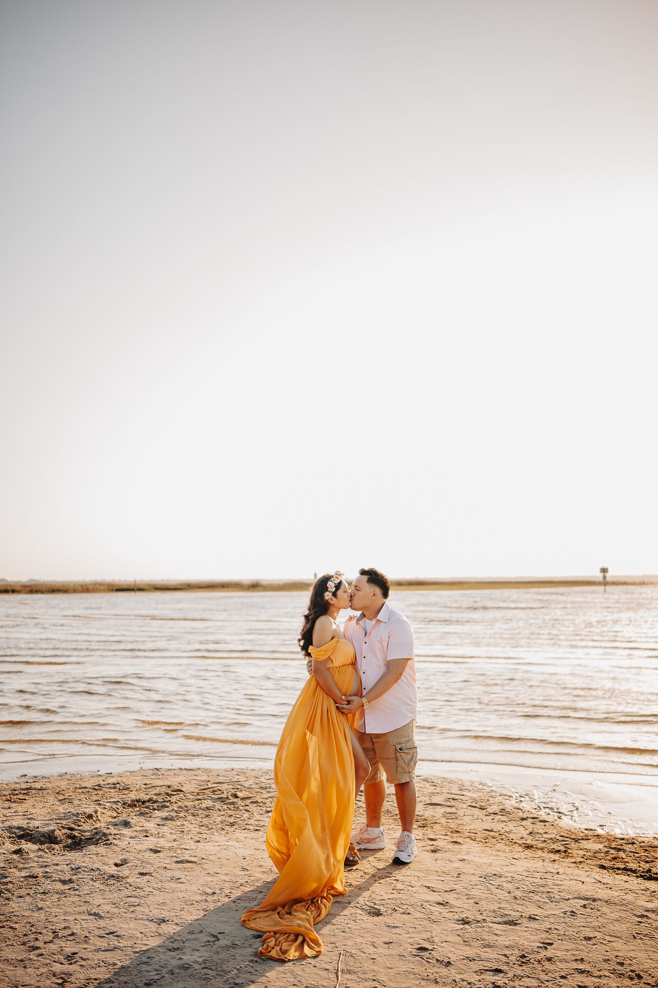 A couple shares a romantic moment at sunset on a sandy beach with calm waters in the background.
